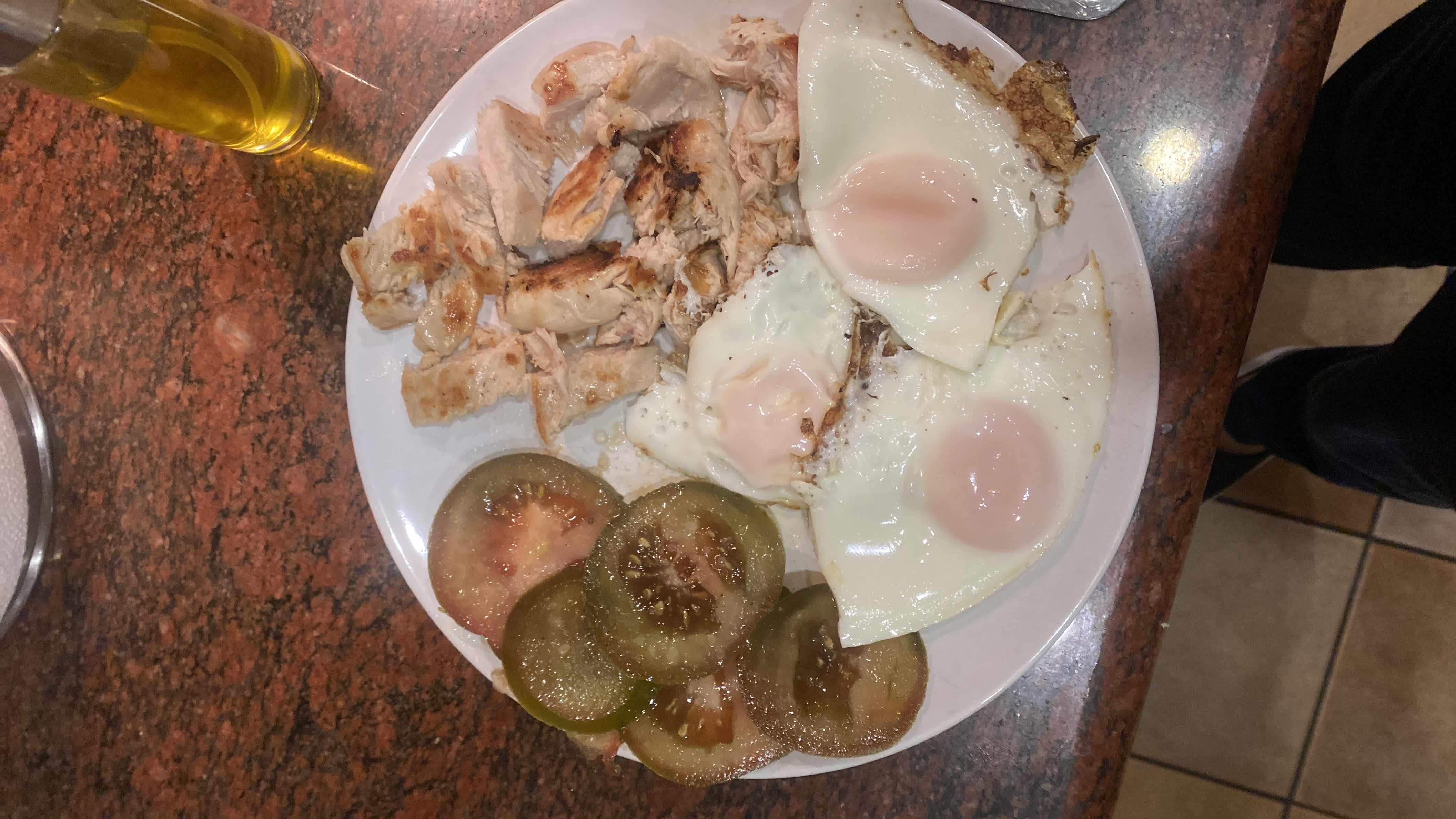 A high-protein meal consisting of grilled chicken breast, fried eggs, sliced green tomatoes, and olive oil, providing a balanced mix of protein, healthy fats, and minimal carbohydrates.