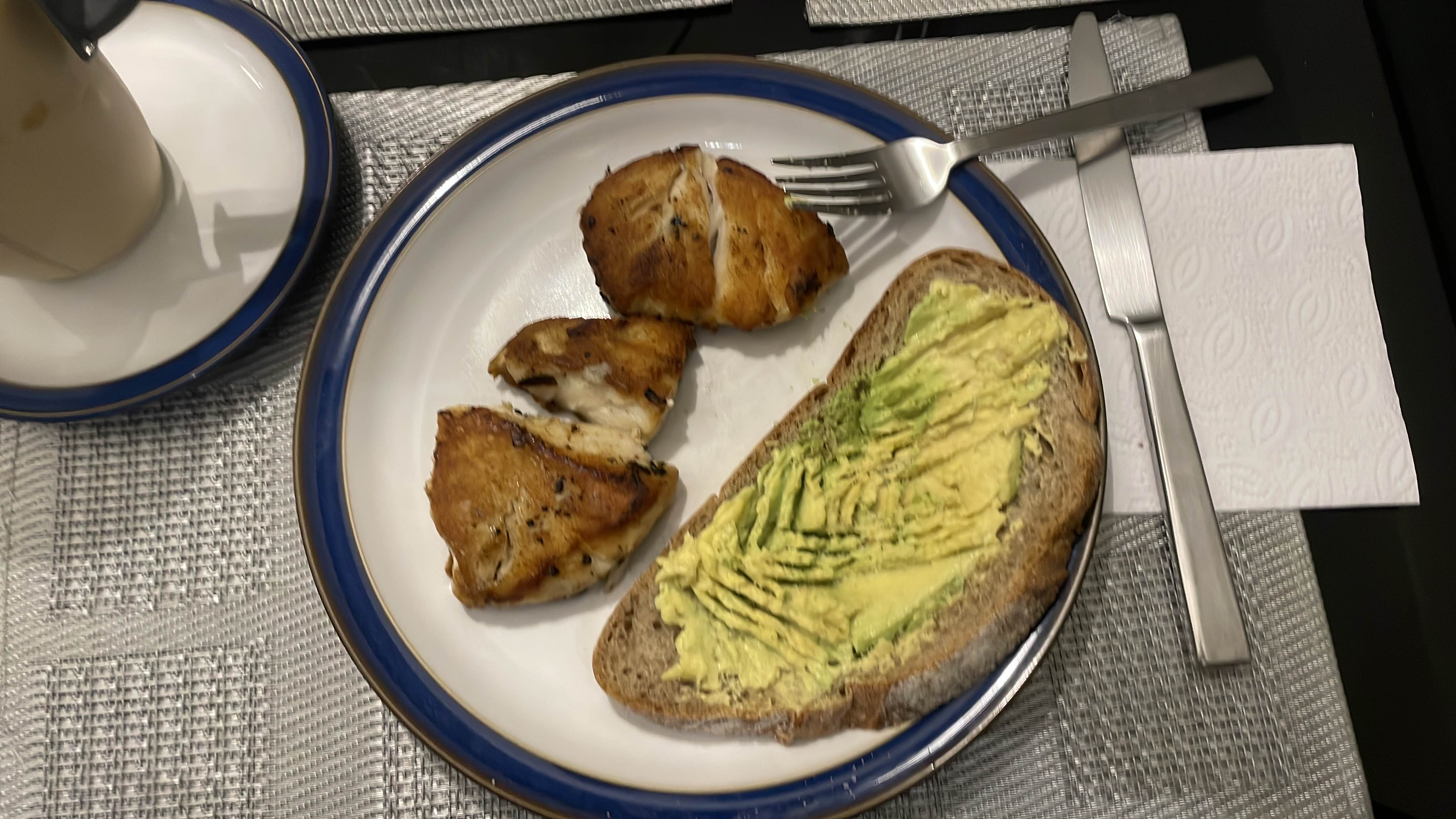 A balanced meal consisting of grilled fish, whole grain bread with mashed avocado, and a cup of coffee.