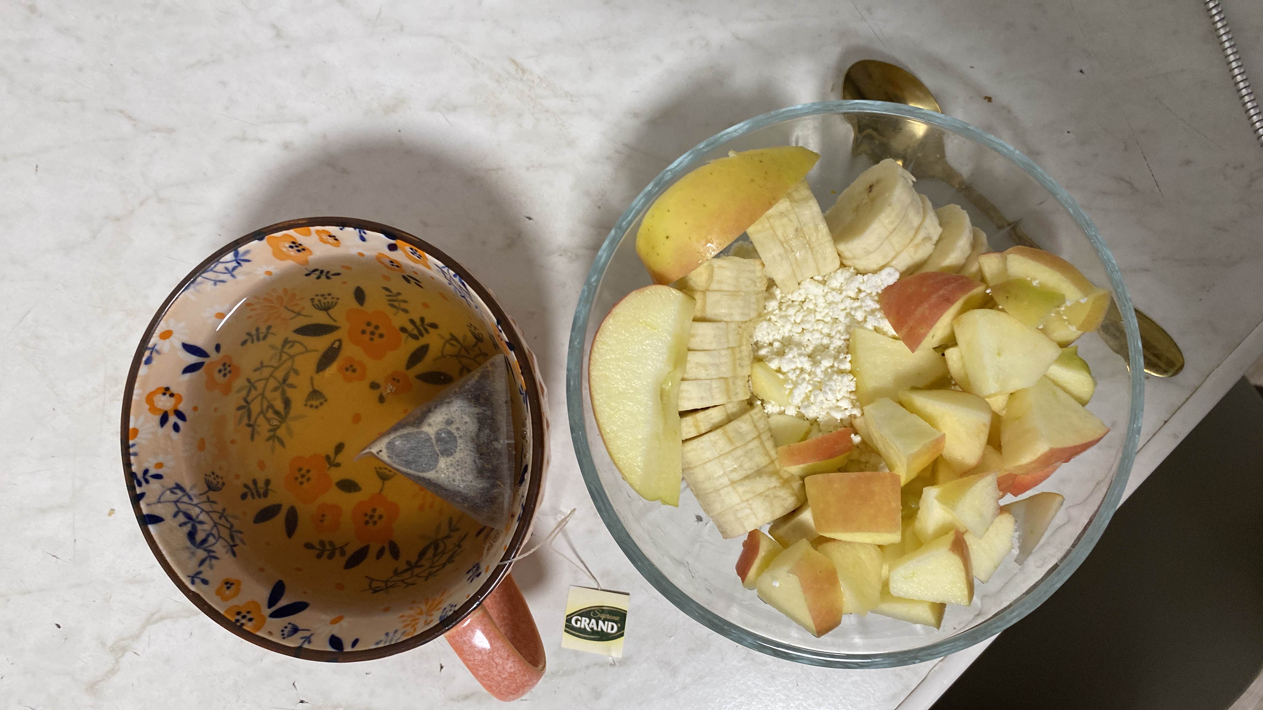 A healthy meal consisting of chopped apples, sliced bananas, and cottage cheese, accompanied by a cup of green tea.