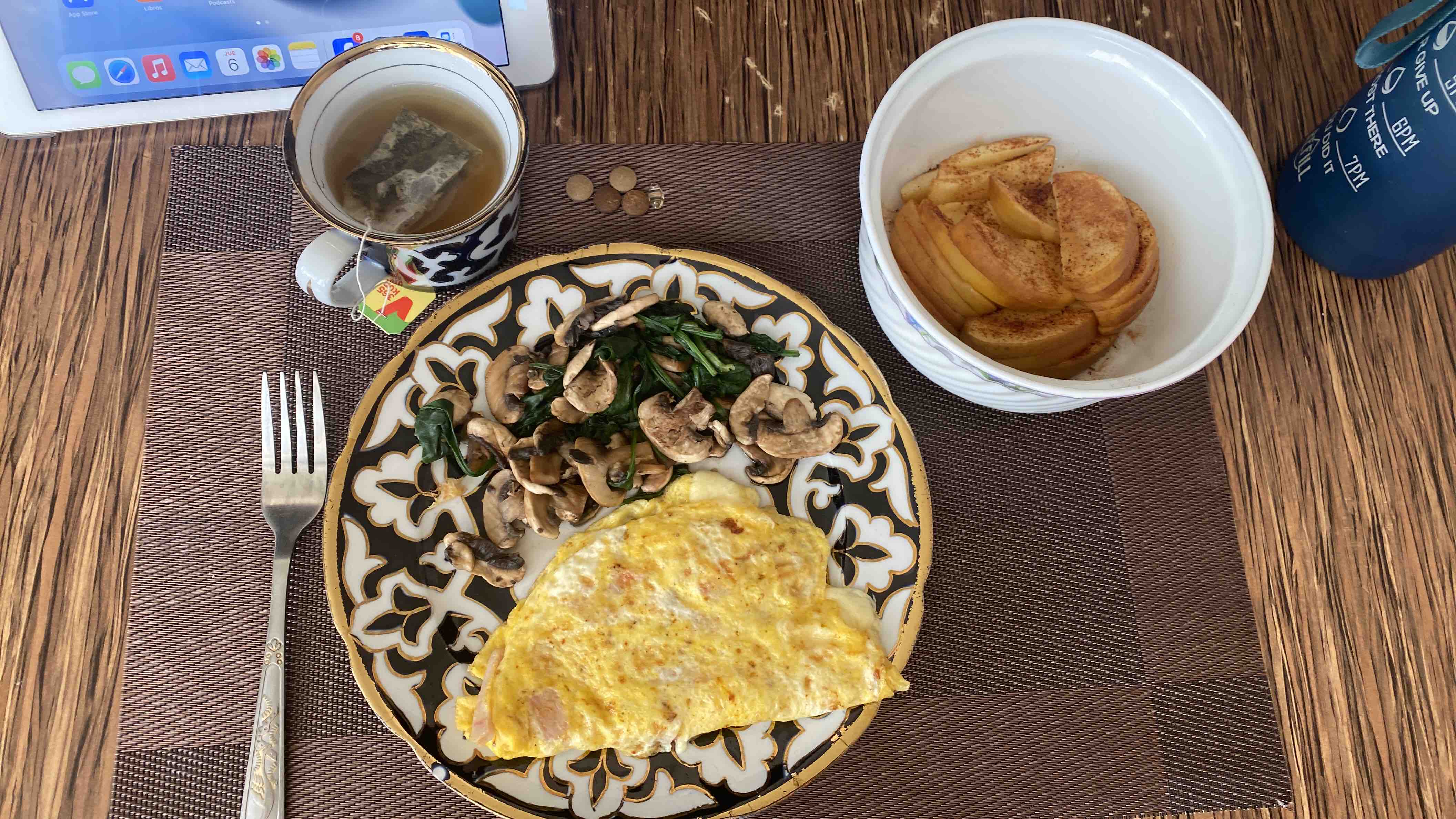 A balanced meal including an omelet with low-fat cheese and ham, sautéed mushrooms and spinach, apple slices with cinnamon, and a cup of tea.