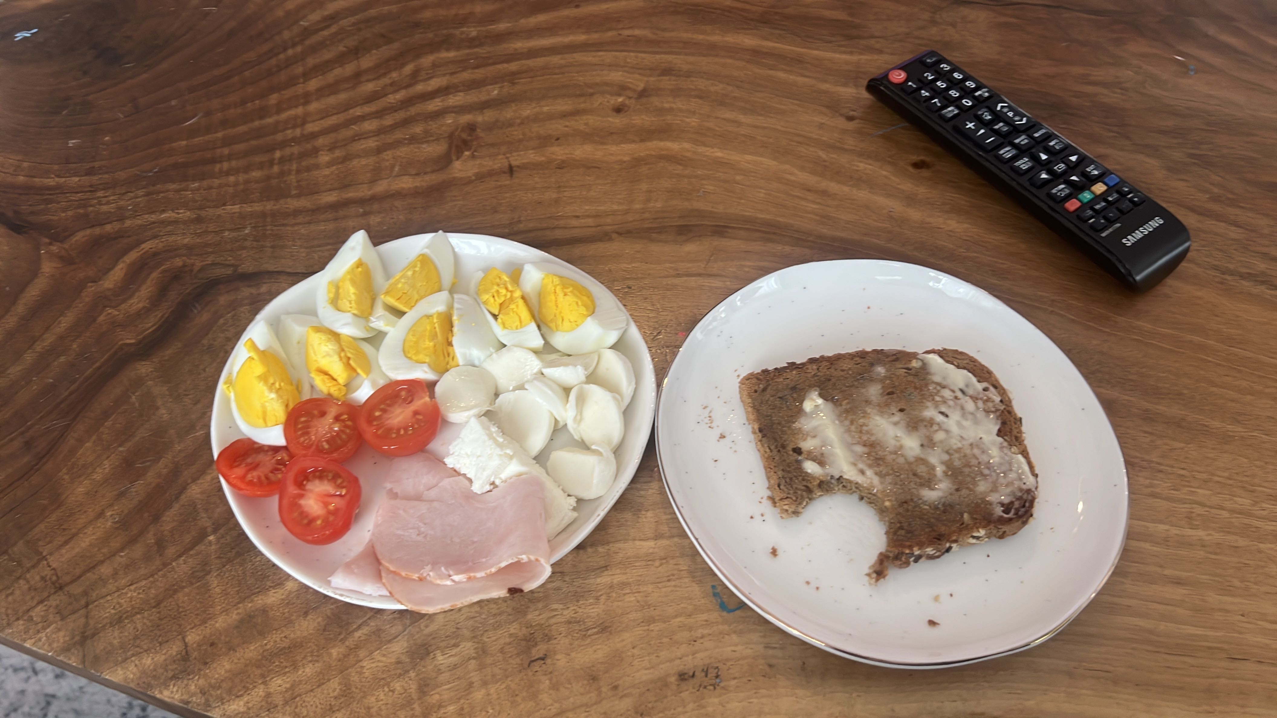 A balanced meal consisting of boiled eggs, mozzarella cheese, ham, tomatoes, and whole grain bread with butter, providing a good mix of protein, fats, and carbohydrates.