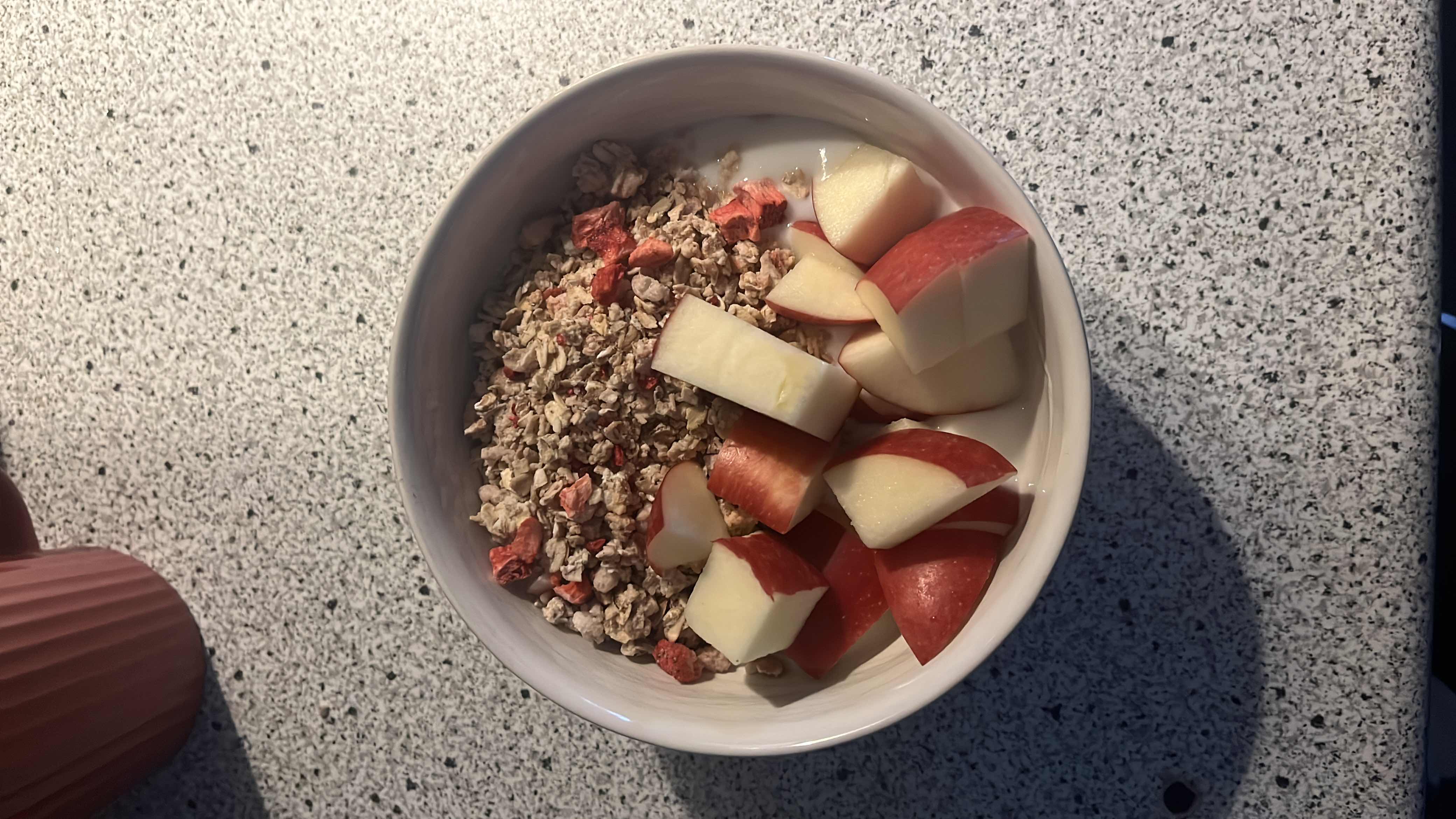 A nutritious bowl containing granola, fresh apple pieces, and milk, providing a balanced mix of carbohydrates, protein, and healthy fats.