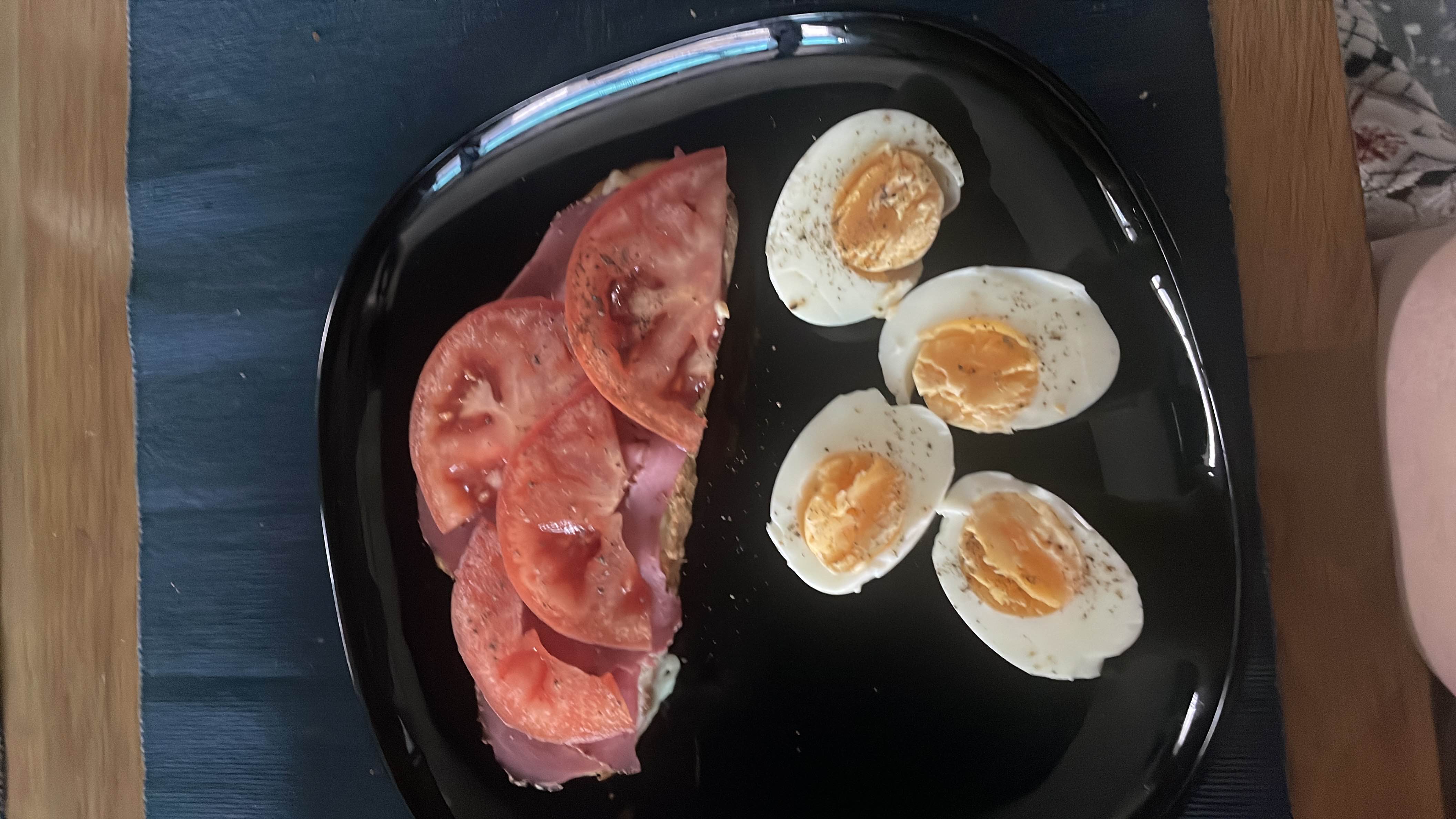 A balanced meal consisting of boiled eggs, whole grain bread with ham, tomato slices, and mayonnaise, providing a good mix of protein, healthy fats, and carbohydrates.