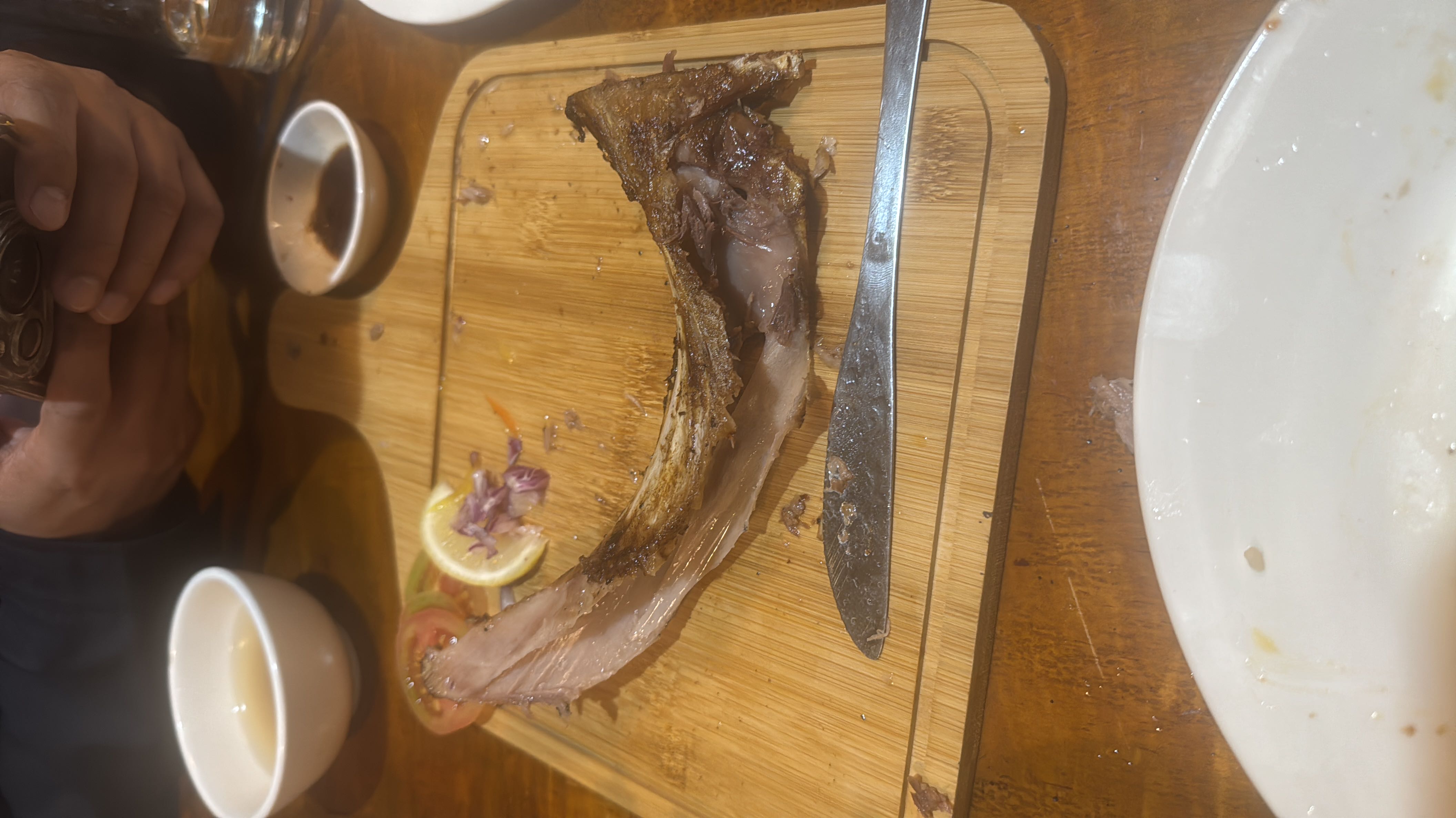 A grilled meat dish served with lemon, onion, and tomato garnishes on a wooden board.