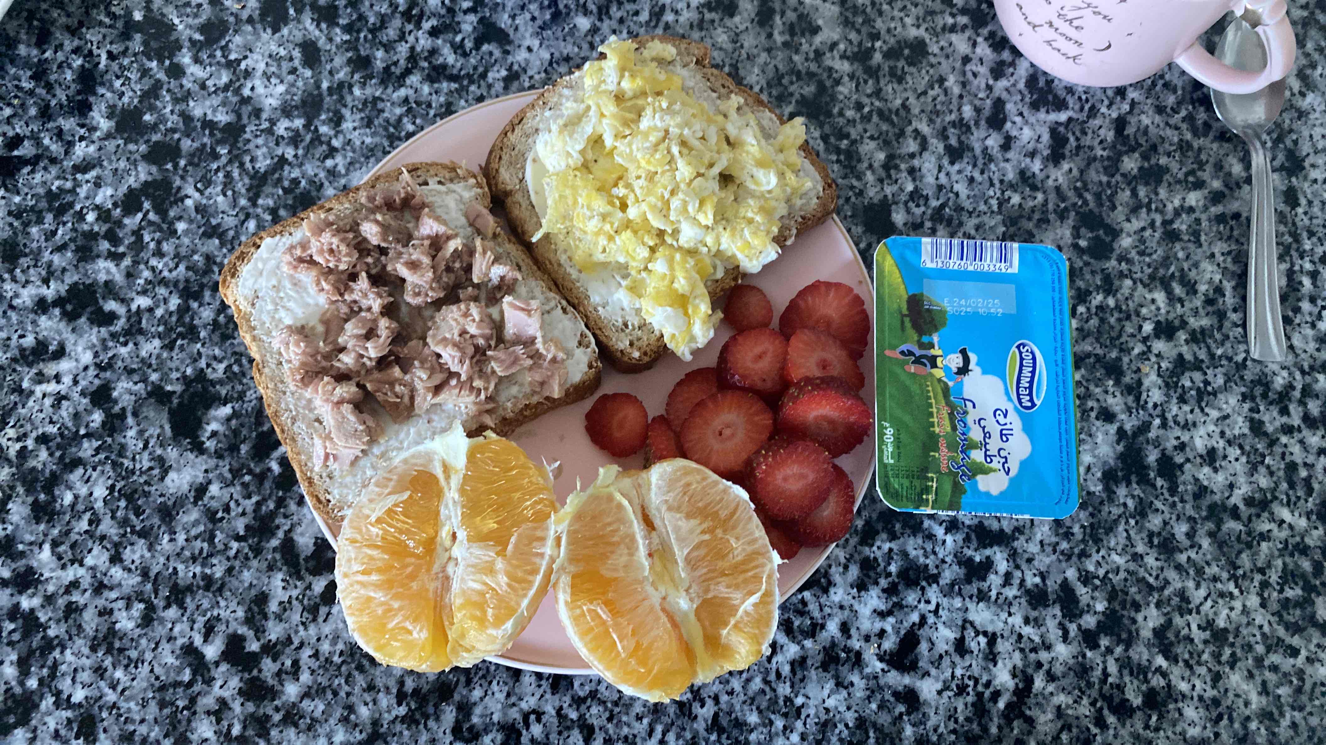 A balanced meal consisting of whole wheat bread with tuna and scrambled eggs, fresh fruits including orange and strawberries, and a portion of cream cheese.