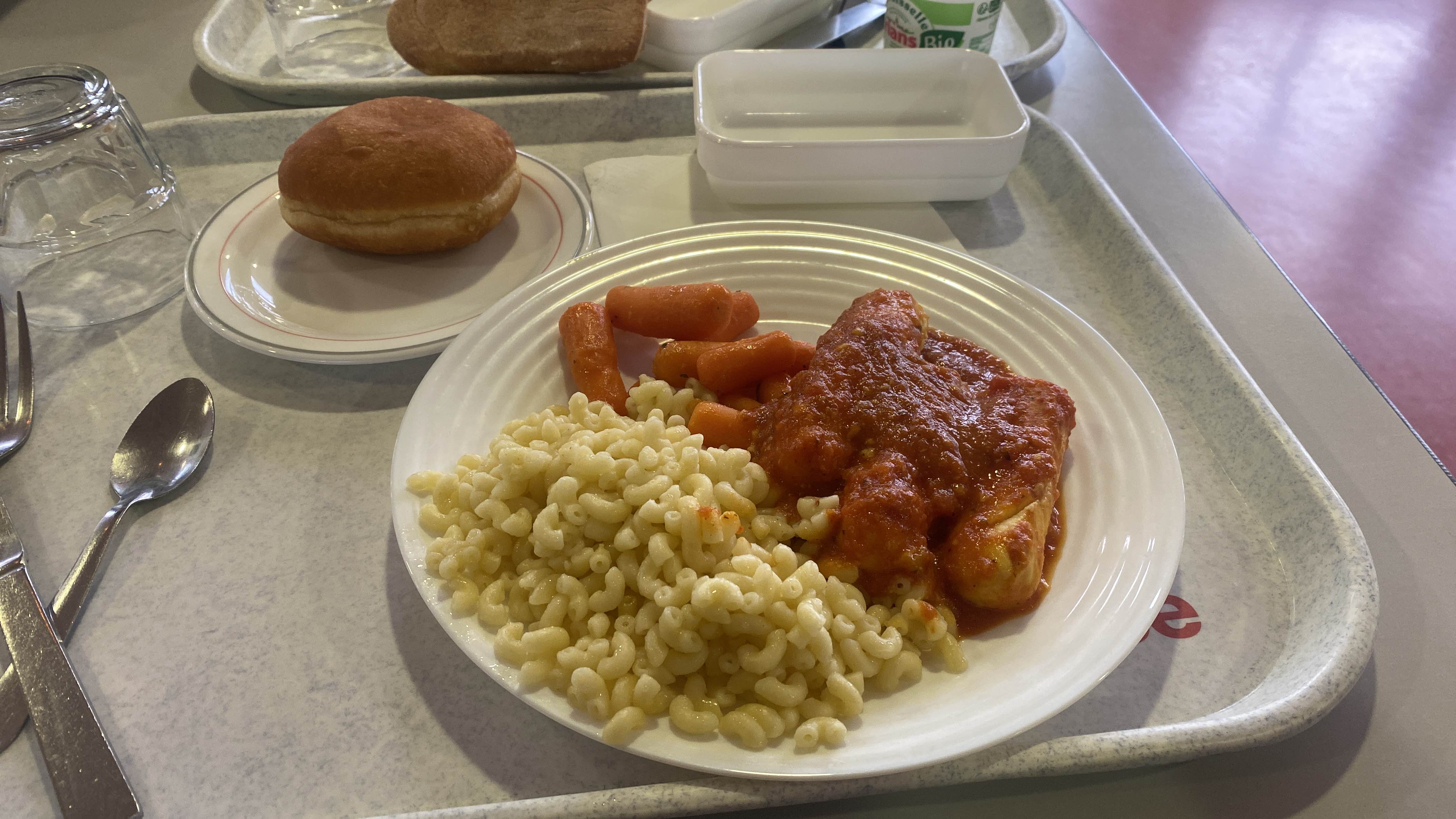 A balanced meal consisting of macaroni, chicken in tomato sauce, cooked carrots, and a bread roll, providing a good mix of protein, carbohydrates, and fats.
