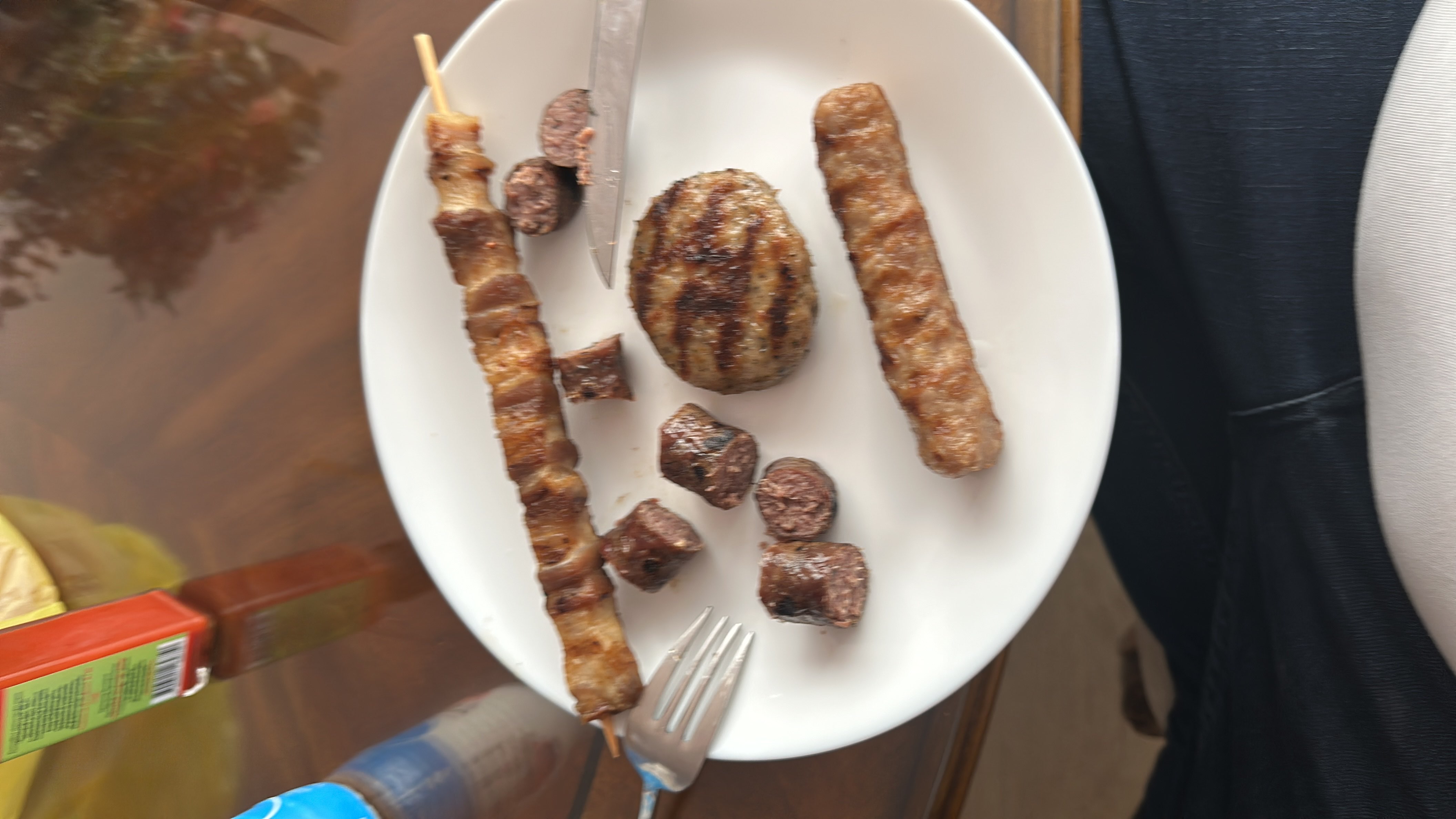 A plate containing various grilled meats, including a skewer, sausage, and burger patty, providing a high-protein and high-fat meal.