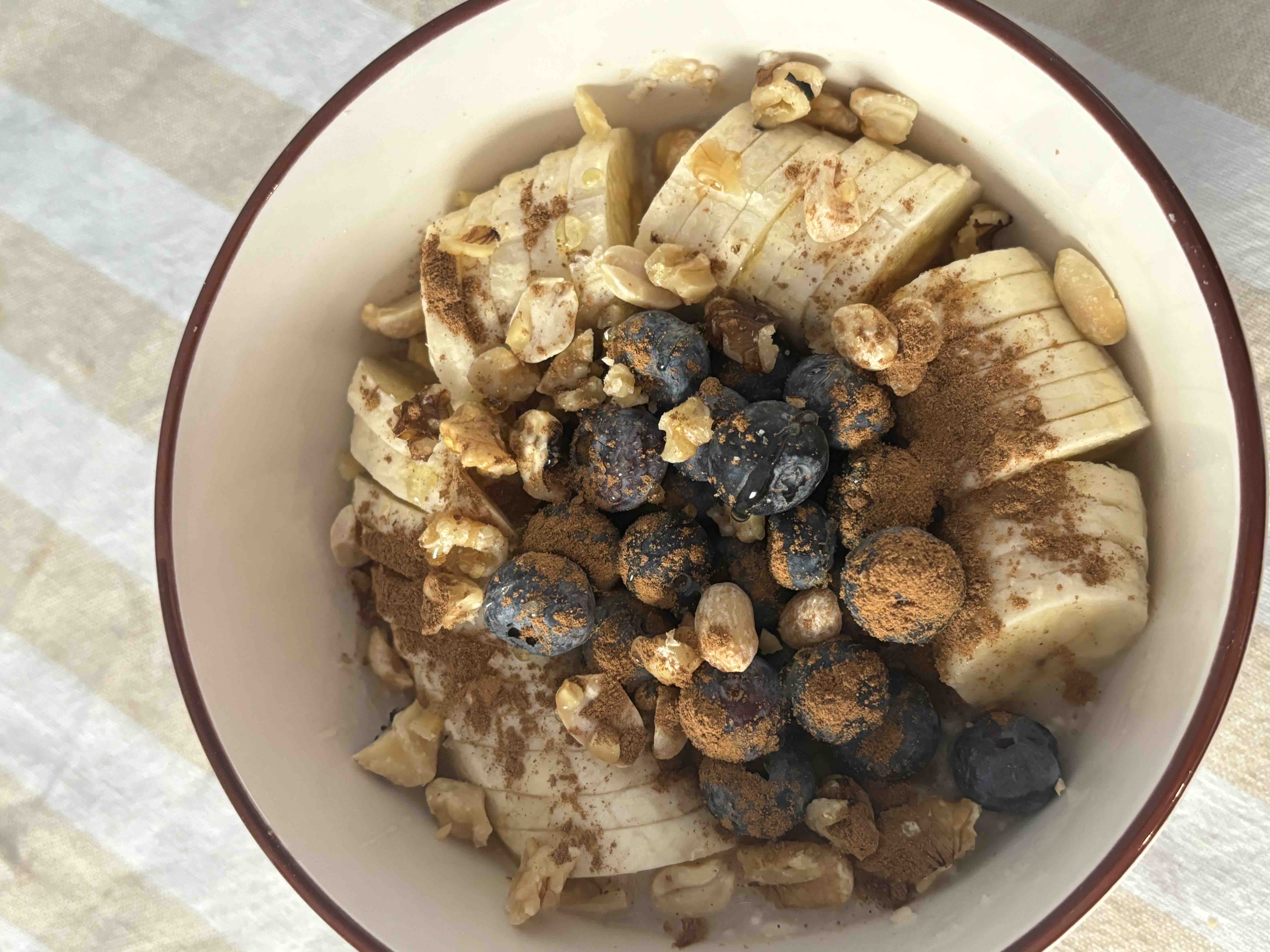 A nutritious bowl containing sliced bananas, blueberries, walnuts, peanuts, and cinnamon, offering a balanced mix of carbohydrates, healthy fats, and protein.