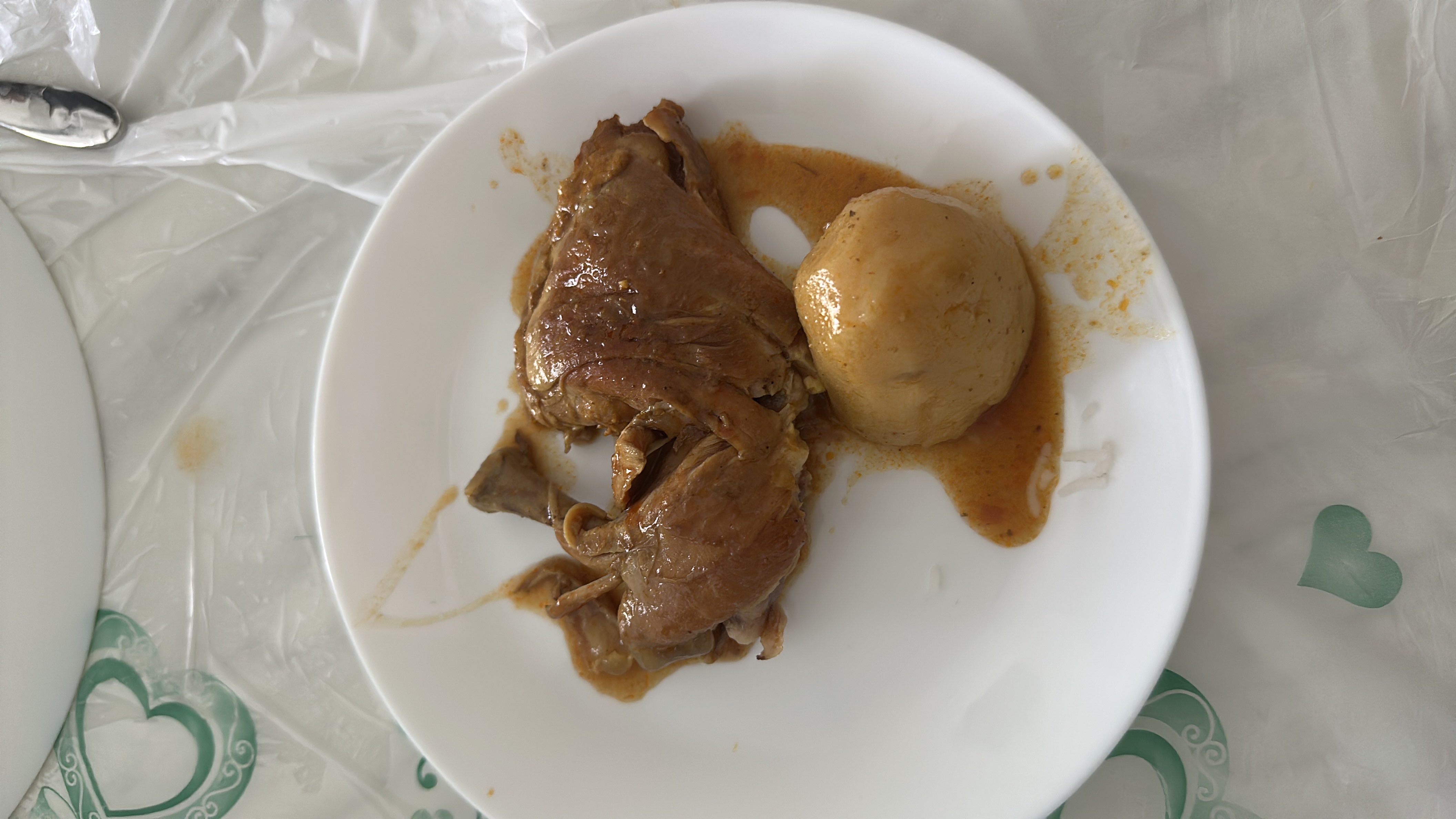 A plate containing braised chicken with a side of a whole cooked potato, served with a flavorful sauce.