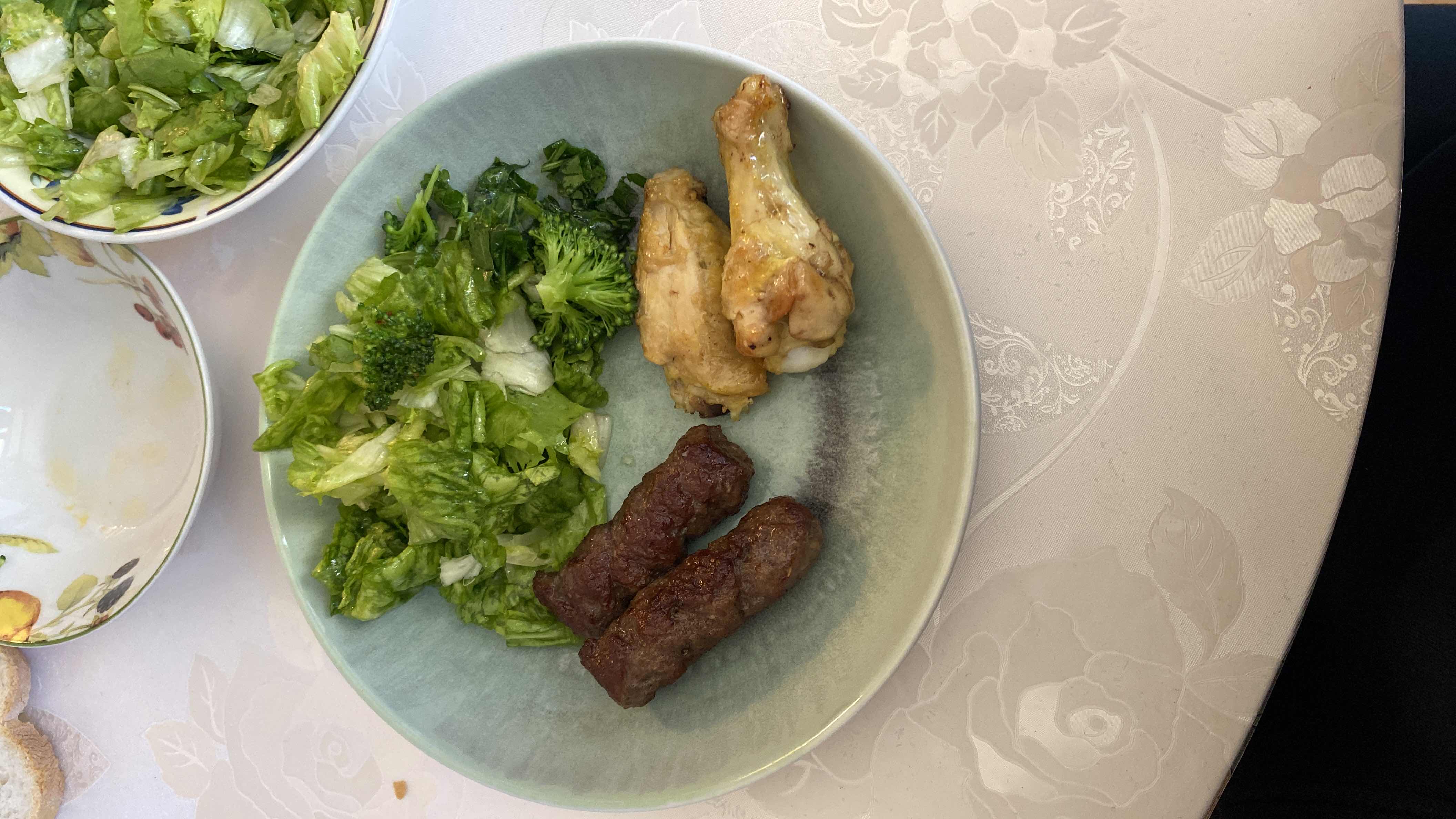 A balanced meal consisting of grilled beef kebabs, chicken wings, and a fresh green salad with broccoli, providing a good mix of protein, fats, and fiber.