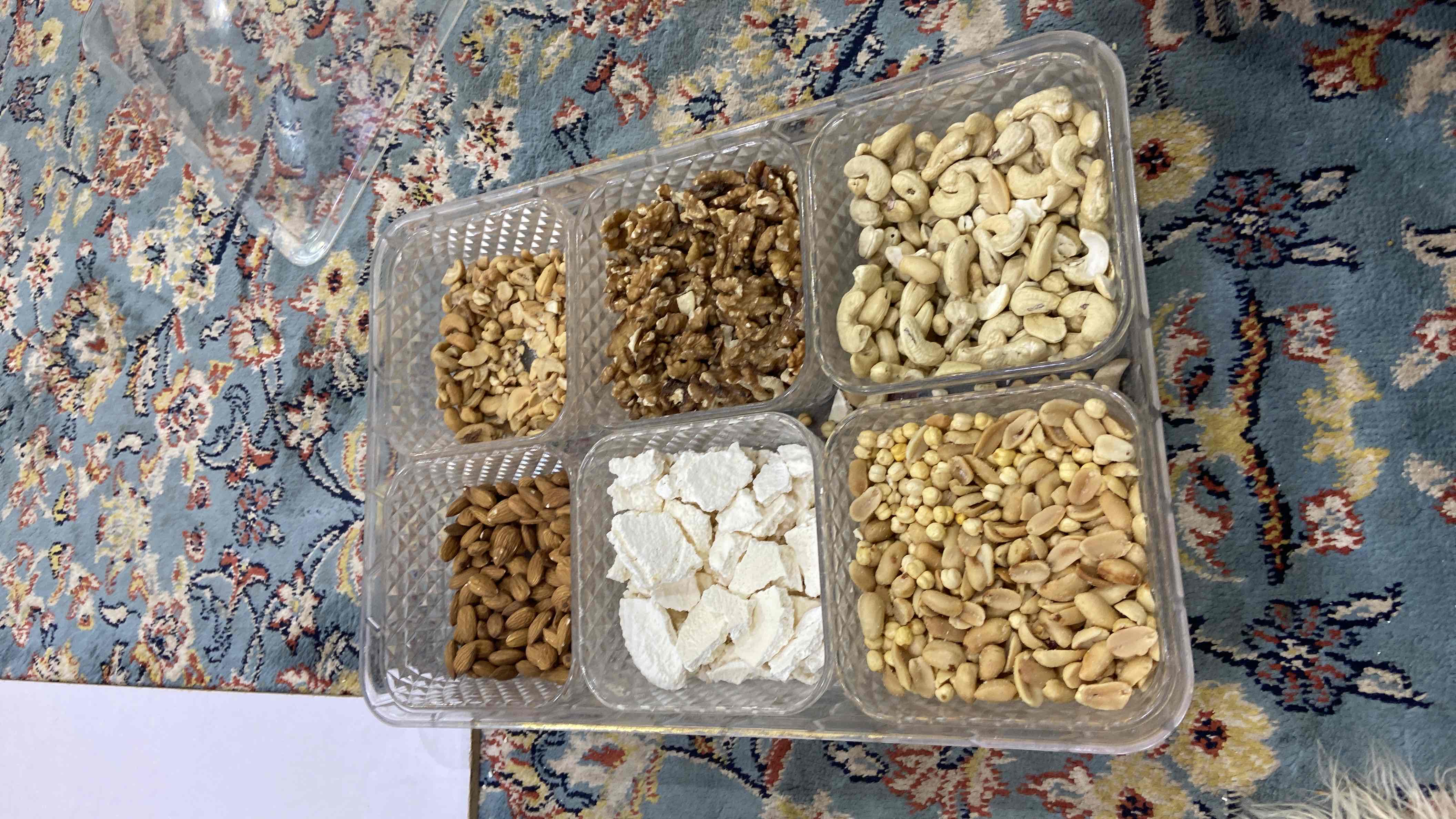 A tray containing a variety of nuts (almonds, cashews, walnuts, peanuts, roasted chickpeas) and sugar candy, providing a high-calorie, protein-rich snack option.