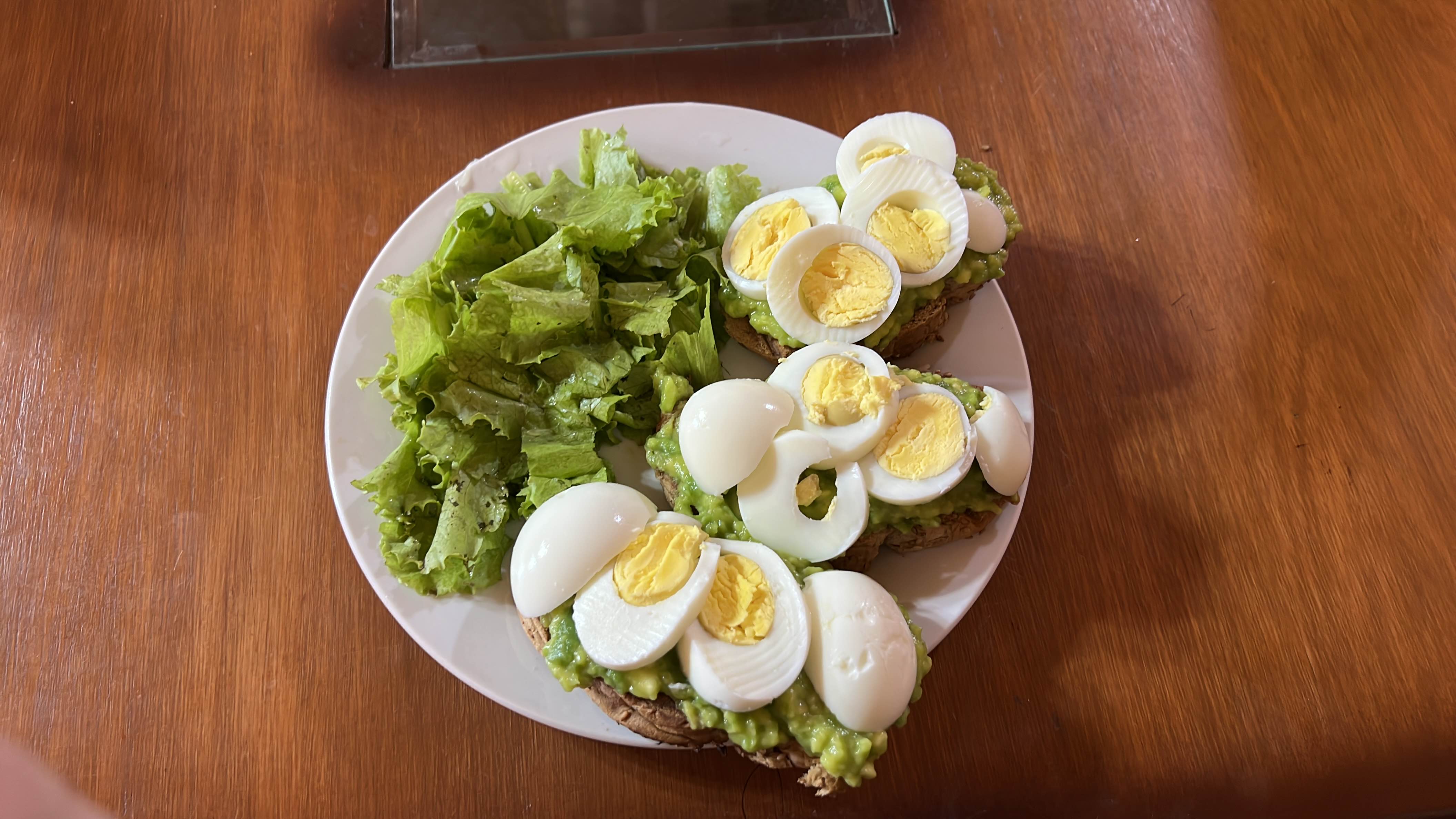 A nutritious meal consisting of whole grain toast topped with mashed avocado and sliced boiled eggs, served with fresh lettuce.