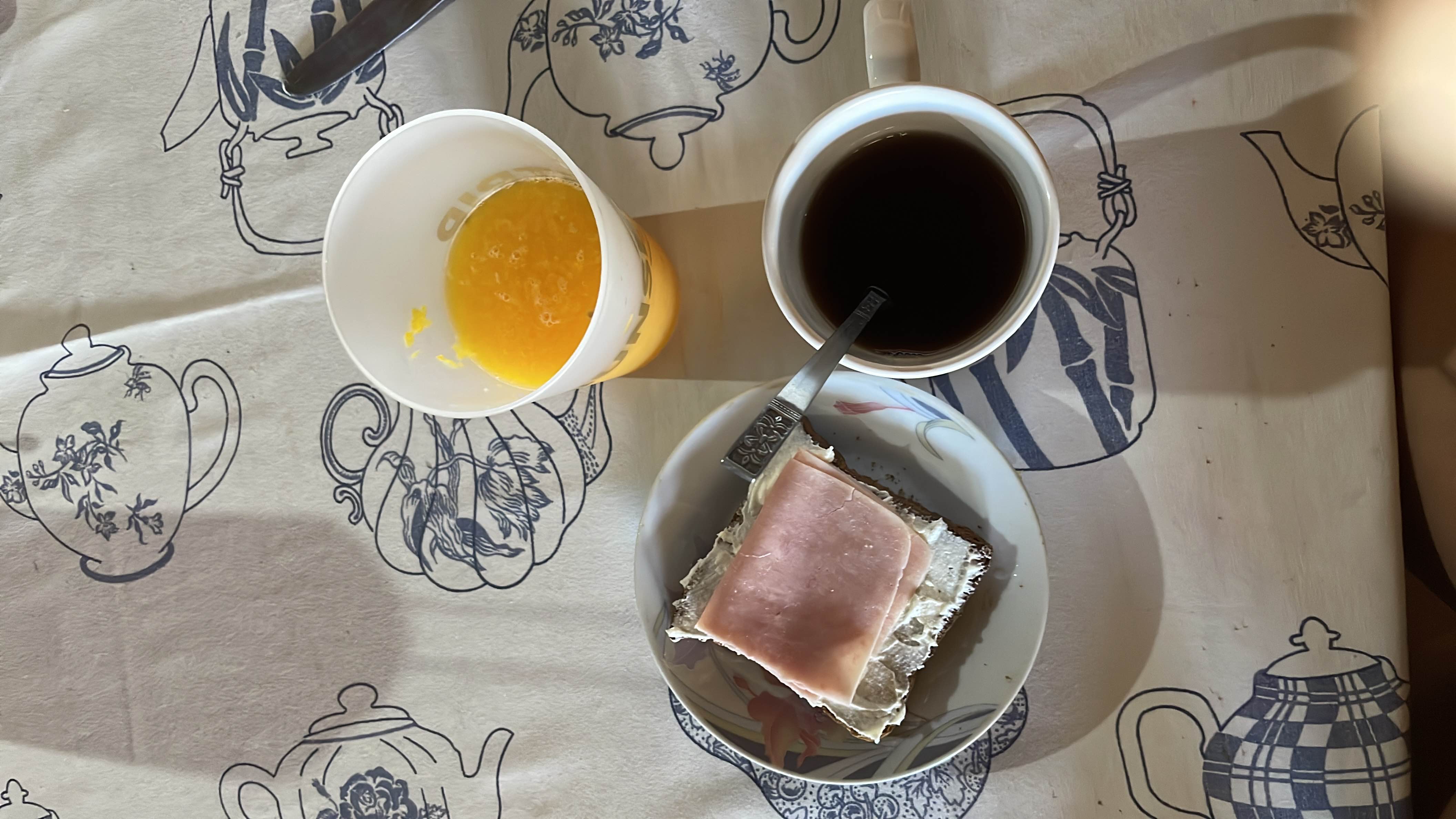 A balanced breakfast consisting of a ham and cream cheese sandwich on whole grain bread, a cup of black coffee, and a glass of fresh orange juice.