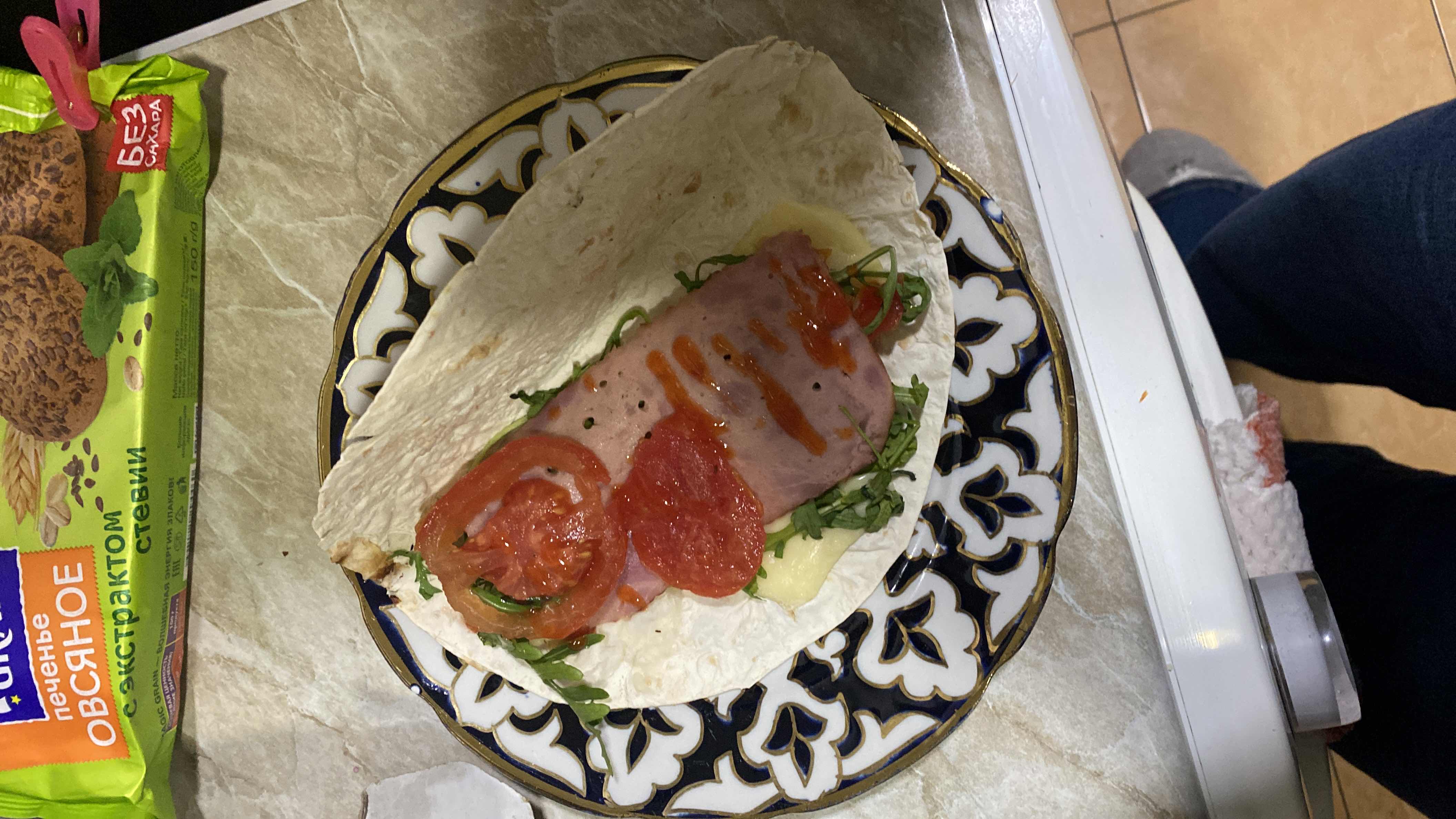 A tortilla wrap with ham, cheese, tomato, arugula, and hot sauce, providing a balanced mix of protein, carbs, and fats.