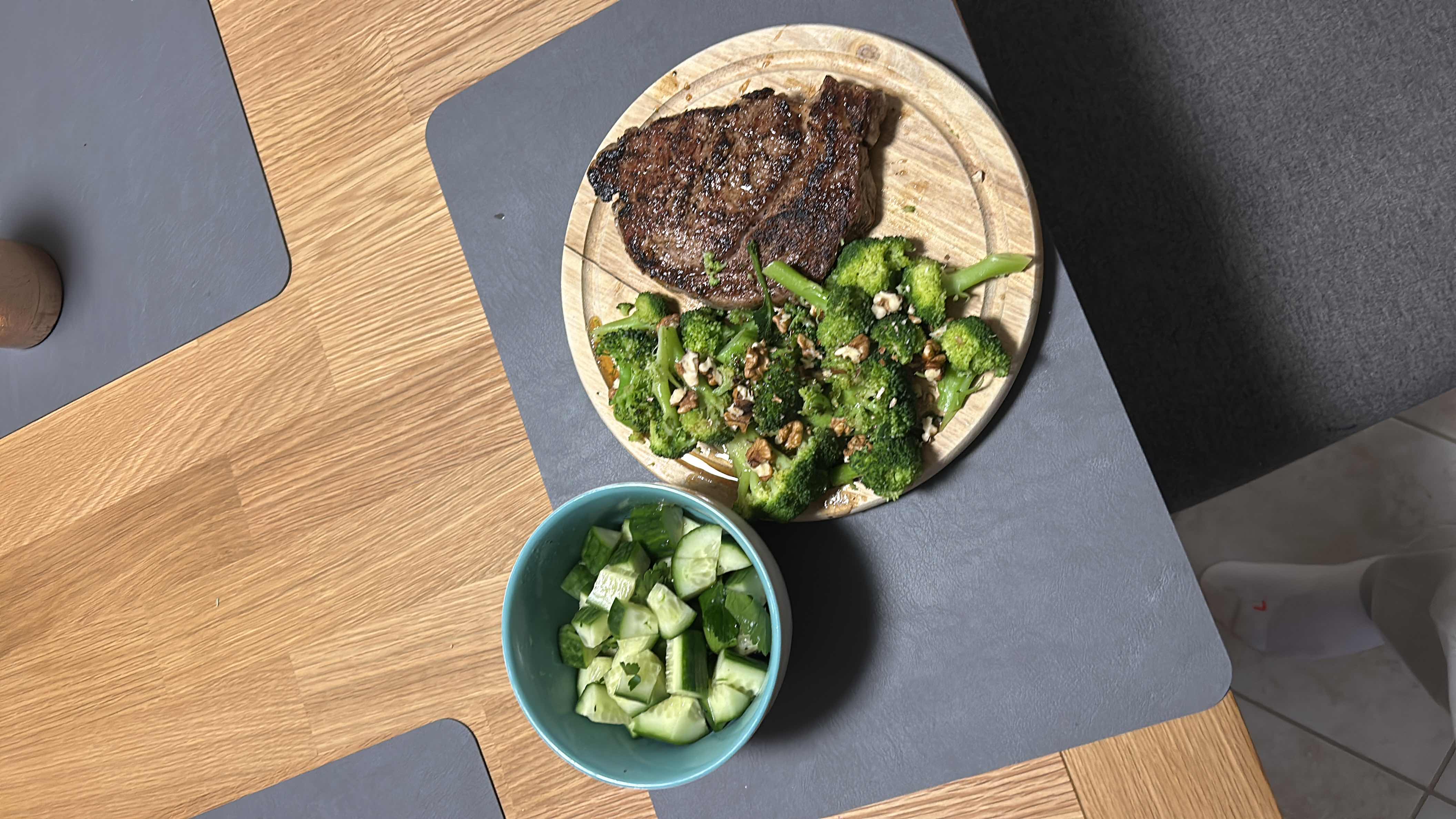 A balanced meal consisting of grilled steak, sautéed broccoli with walnuts, and a side of fresh cucumber salad.