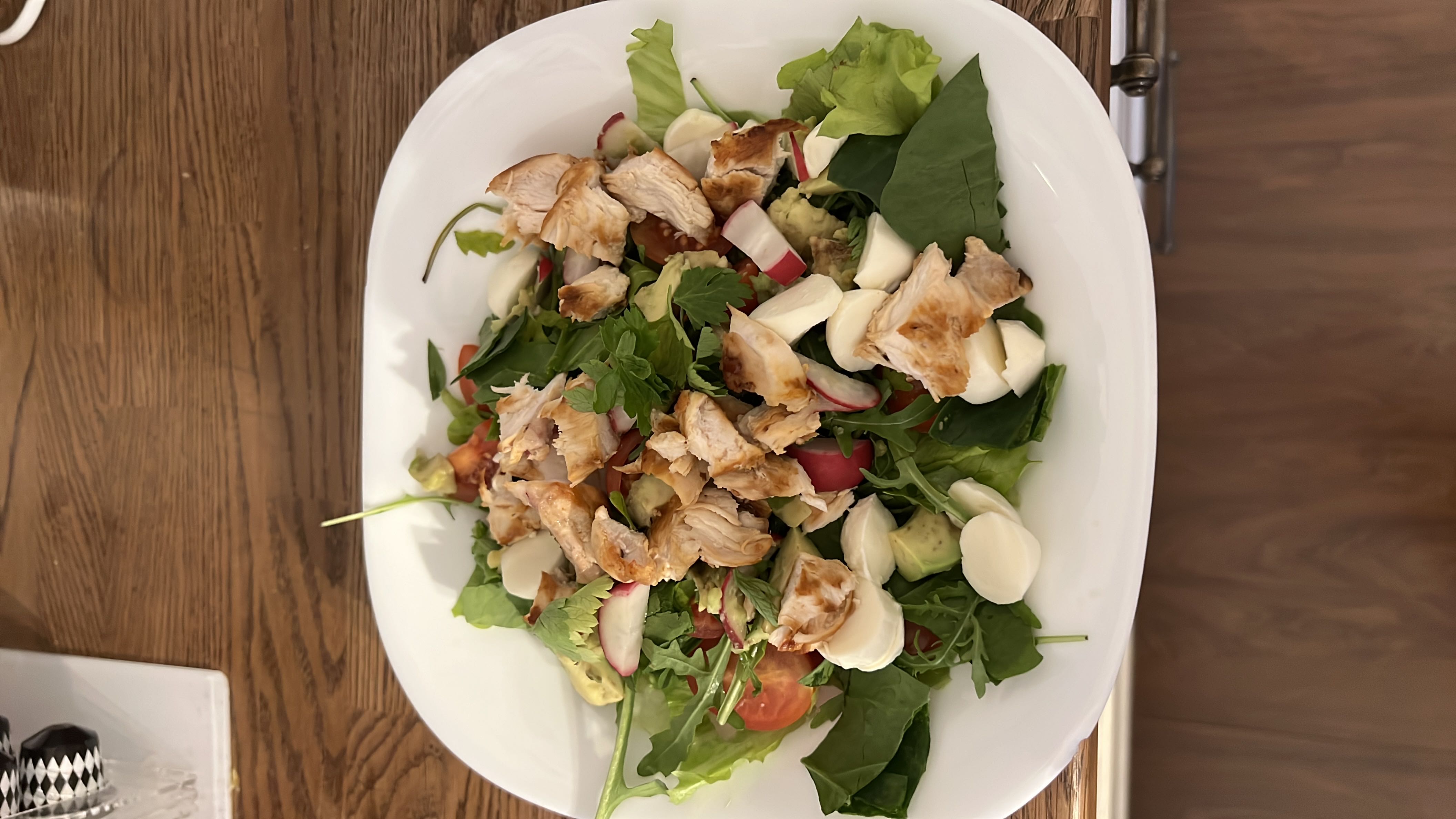 A fresh and healthy salad with grilled chicken, mixed greens, cherry tomatoes, mozzarella cheese, radishes, and avocado.