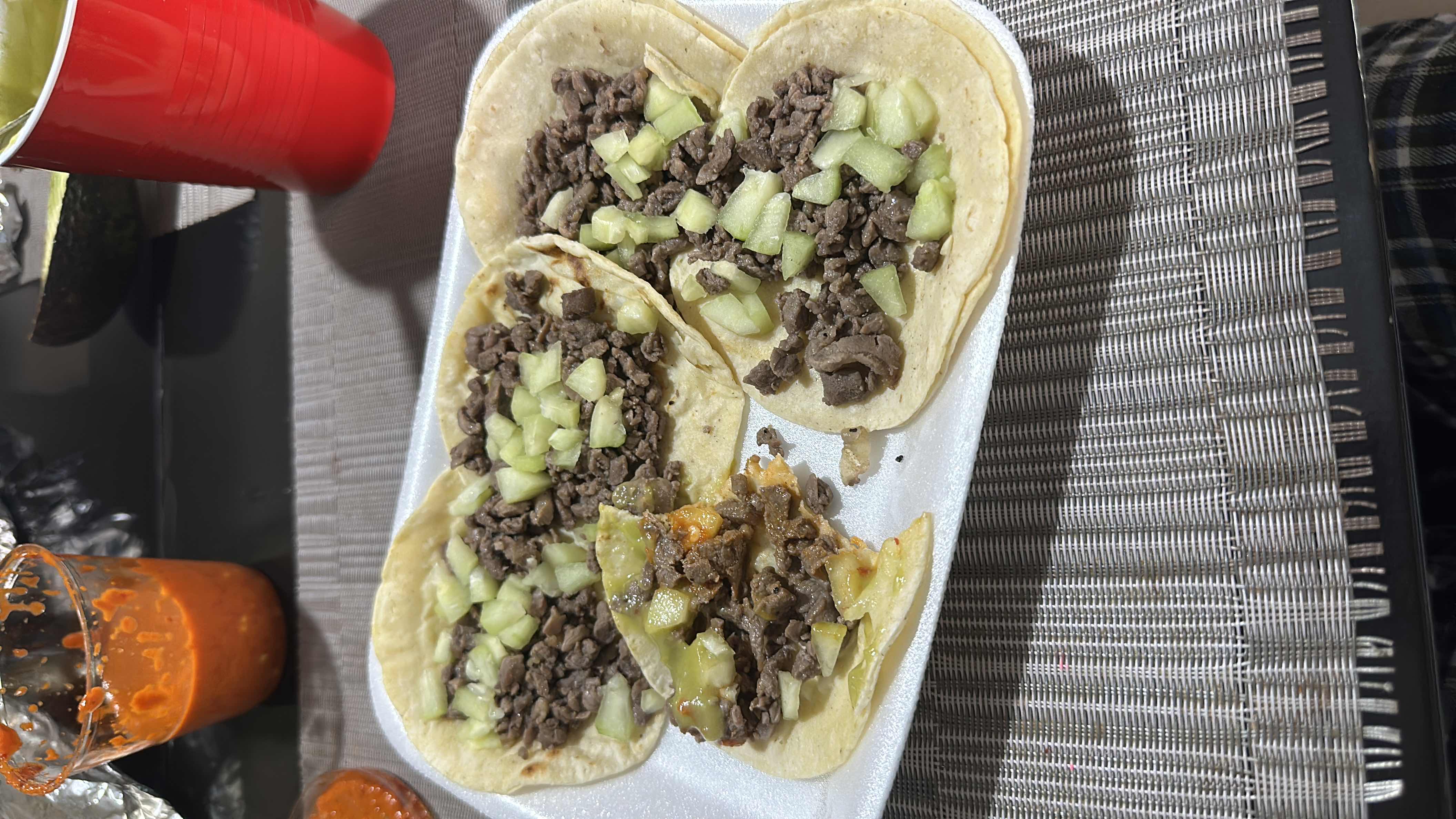 A plate of four beef tacos served on corn tortillas, topped with diced cucumber and accompanied by guacamole and salsa.