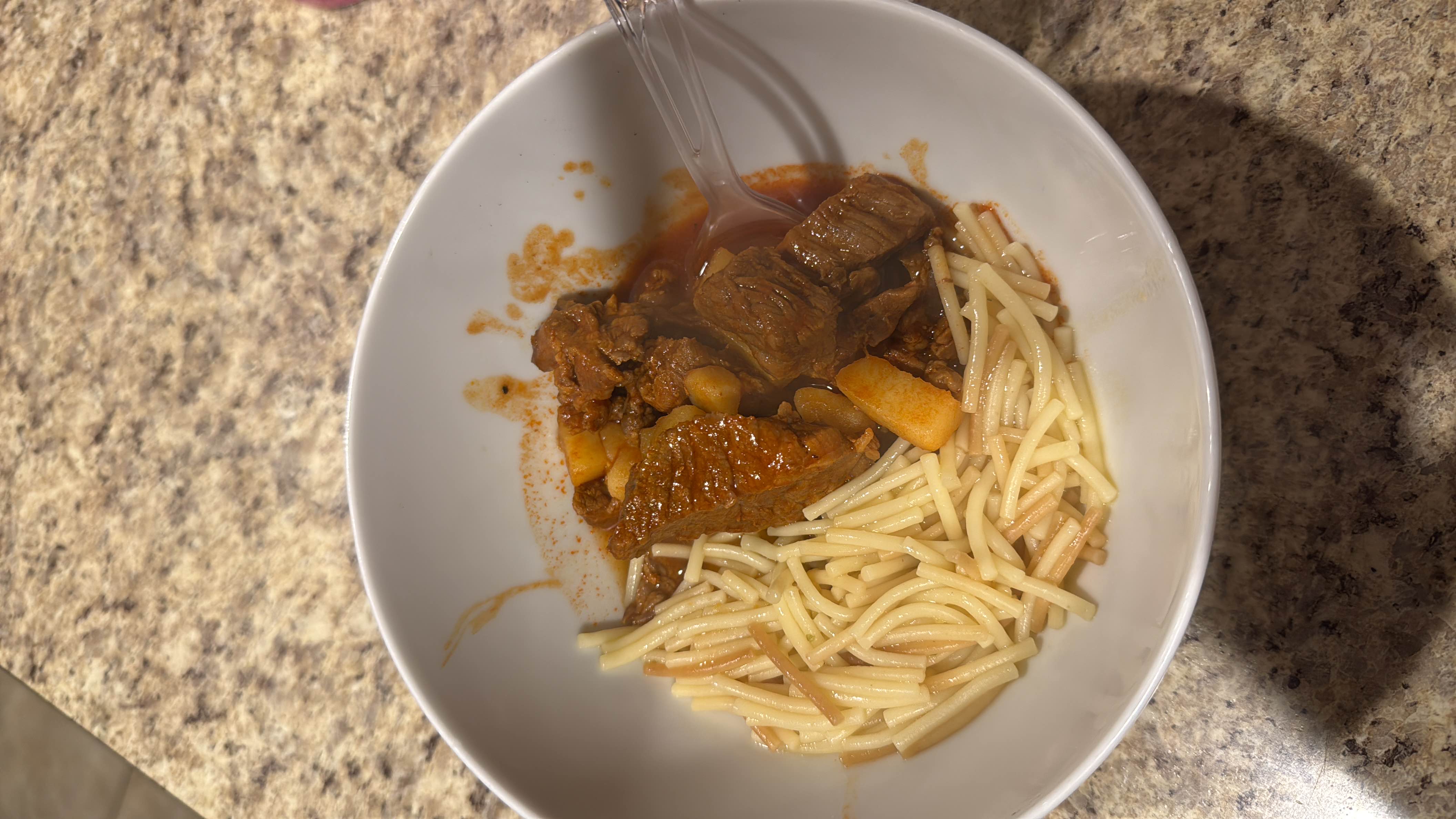 A hearty dish consisting of beef stew with potatoes in a tomato-based sauce, served alongside vermicelli pasta.