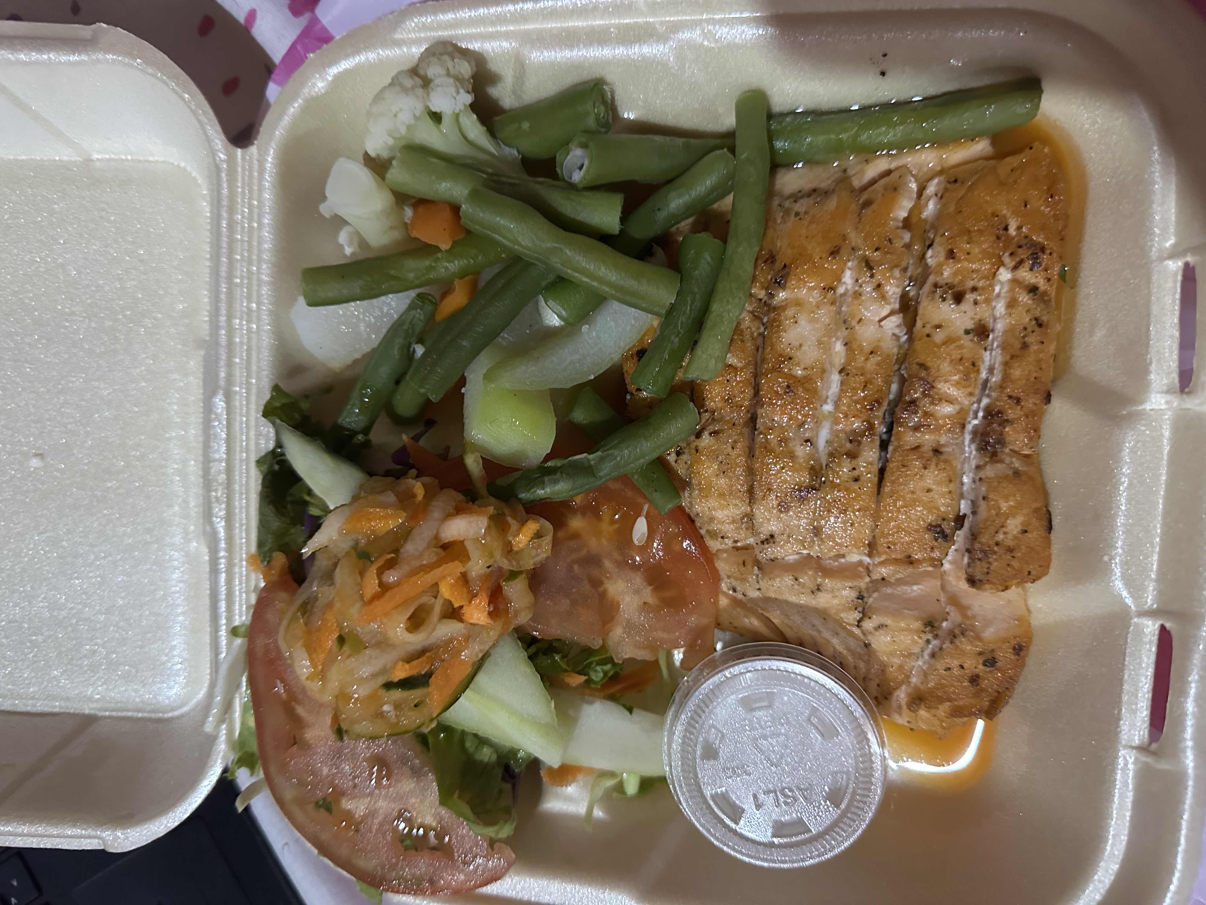 A healthy meal consisting of grilled salmon, fresh vegetables including green beans, tomatoes, lettuce, carrots, and cauliflower, served with a light dressing.
