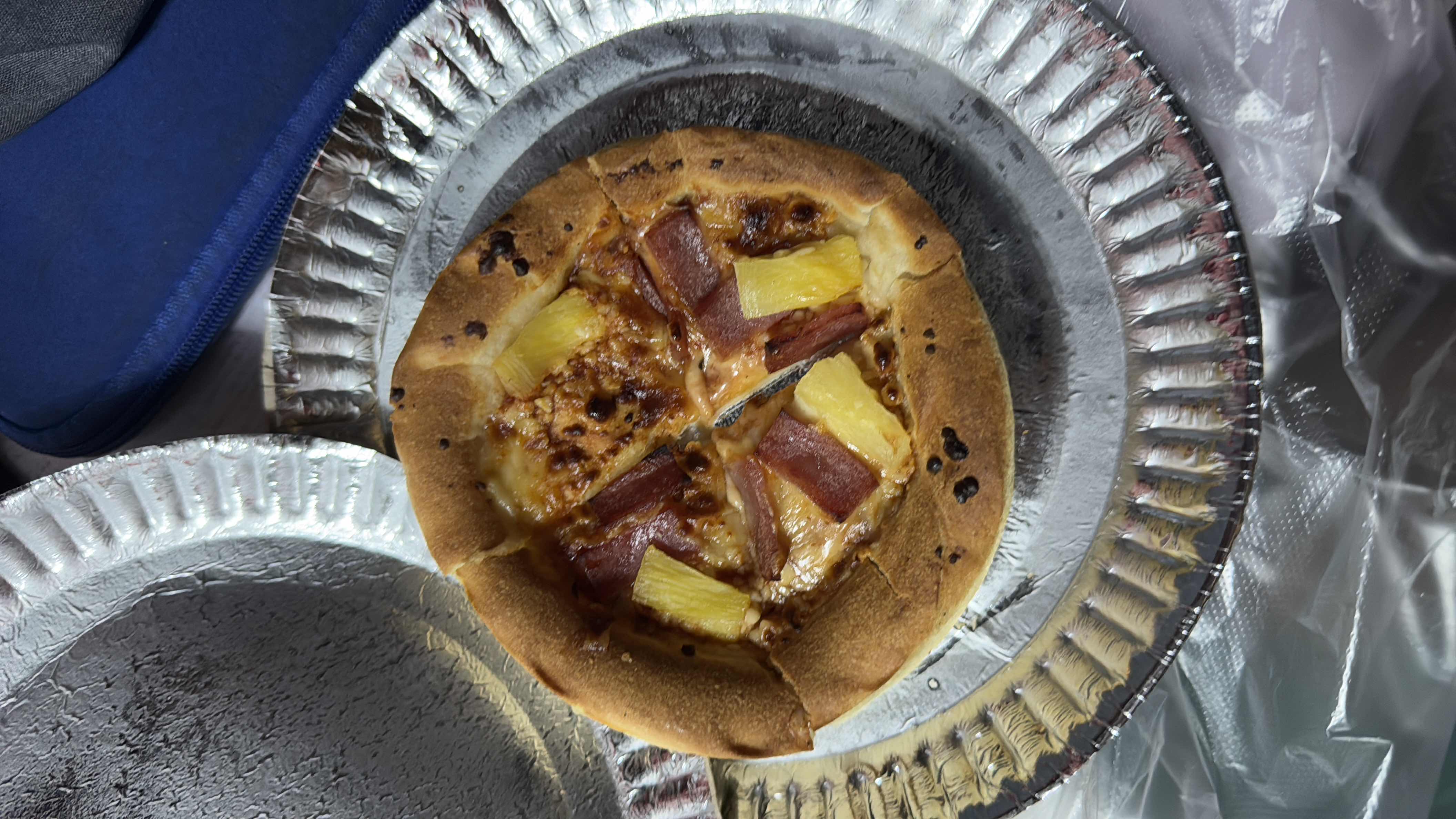 A small Hawaiian-style pizza with a thick crust, topped with cheese, ham, and pineapple.