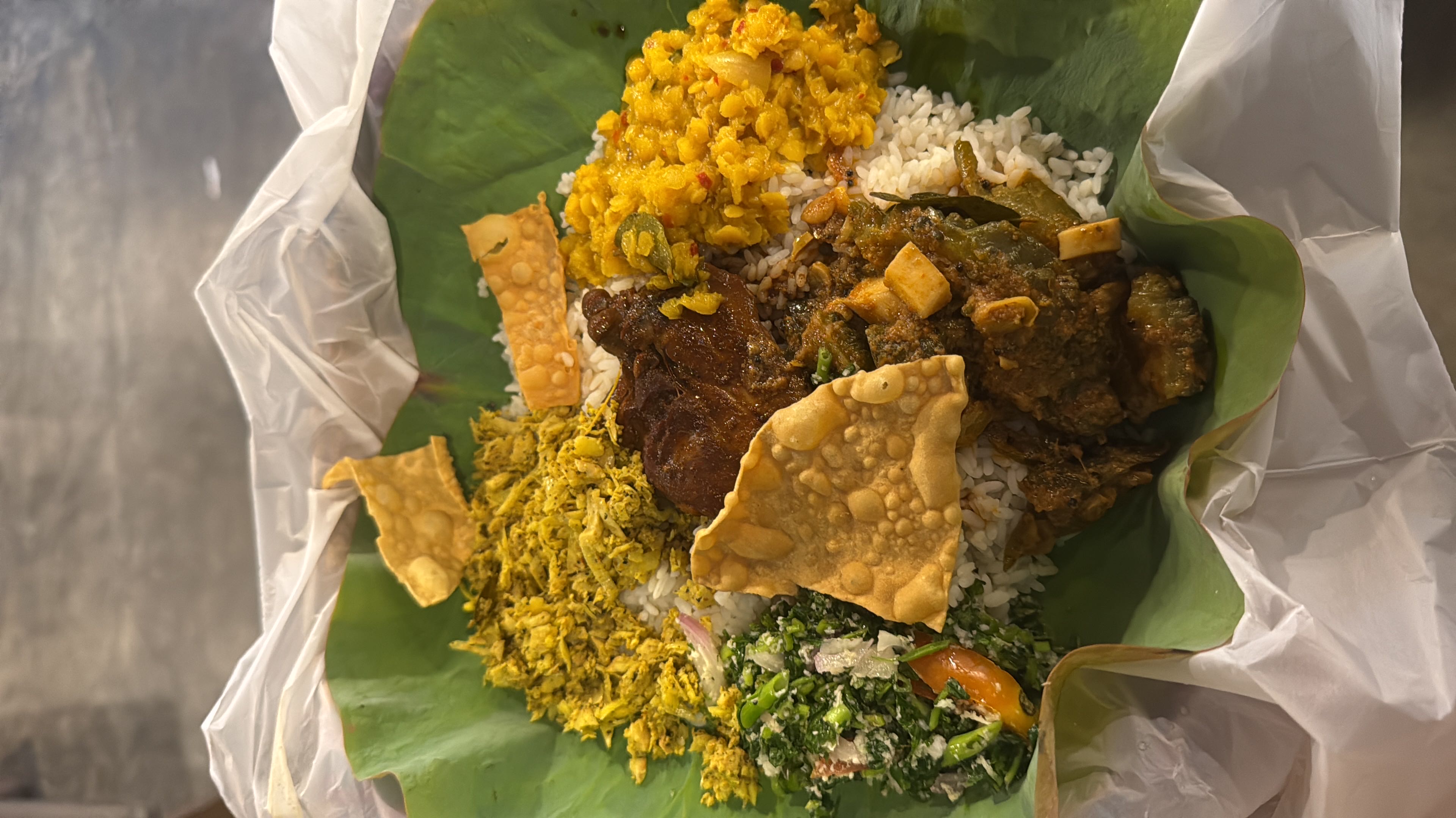 A traditional banana leaf meal featuring rice, chicken curry, lentils, shredded chicken, leafy greens salad, and crispy papadam, offering a balanced mix of protein, carbs, and fats.