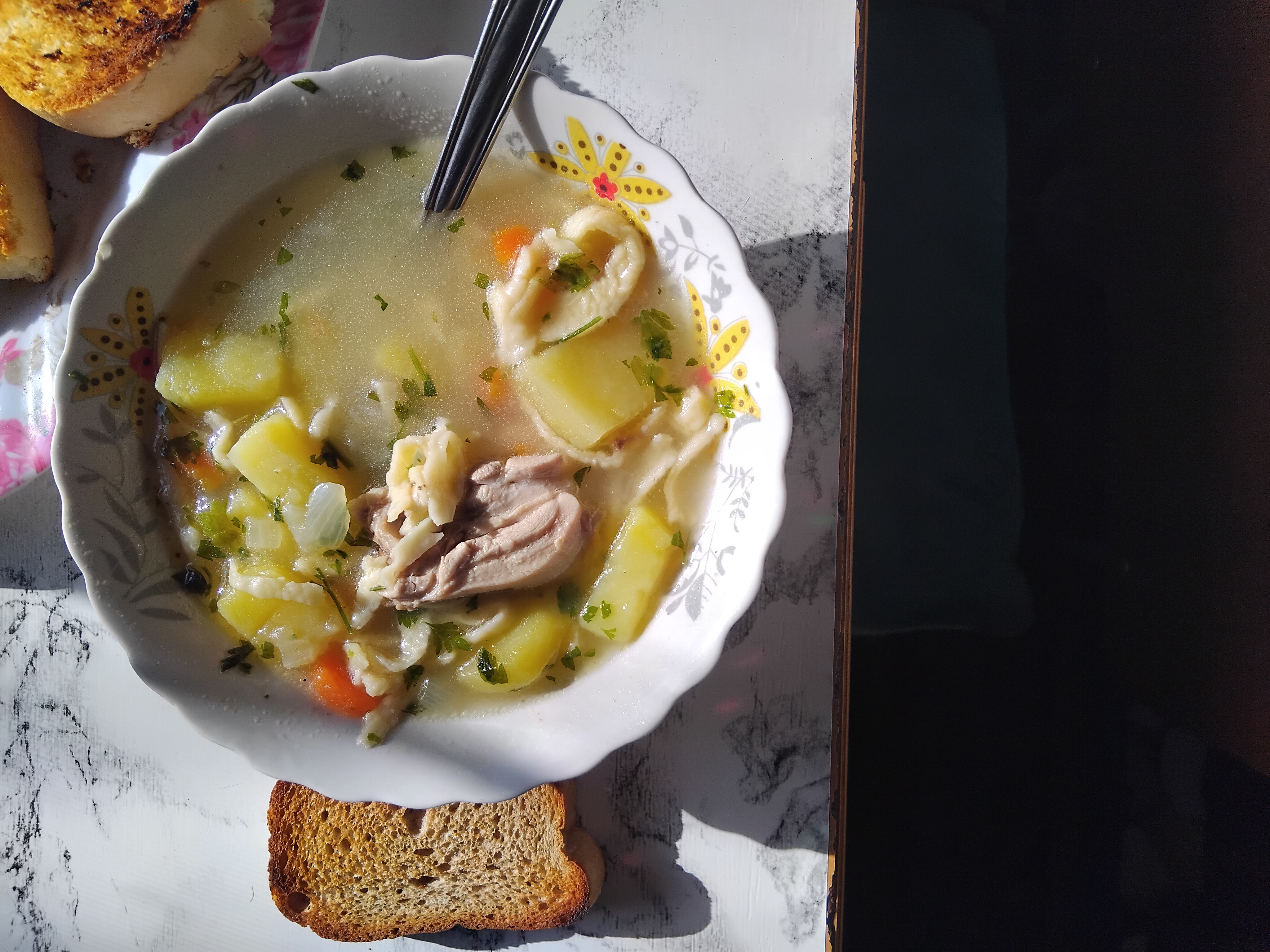 A hearty homemade chicken soup with potatoes, carrots, and onions in a flavorful broth, served with toasted bread.