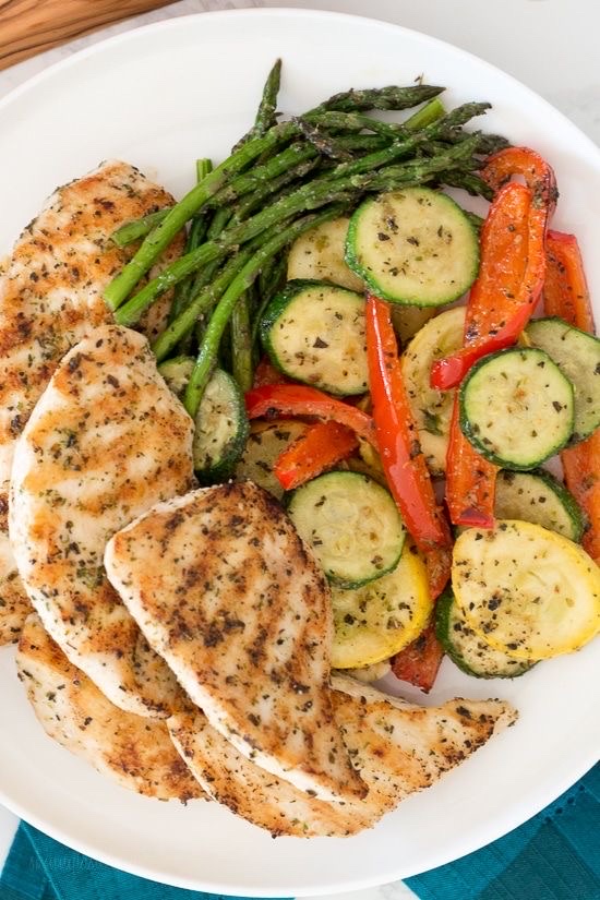 A healthy grilled chicken dish served with a mix of roasted vegetables including zucchini, bell peppers, squash, and asparagus, seasoned with herbs and olive oil.