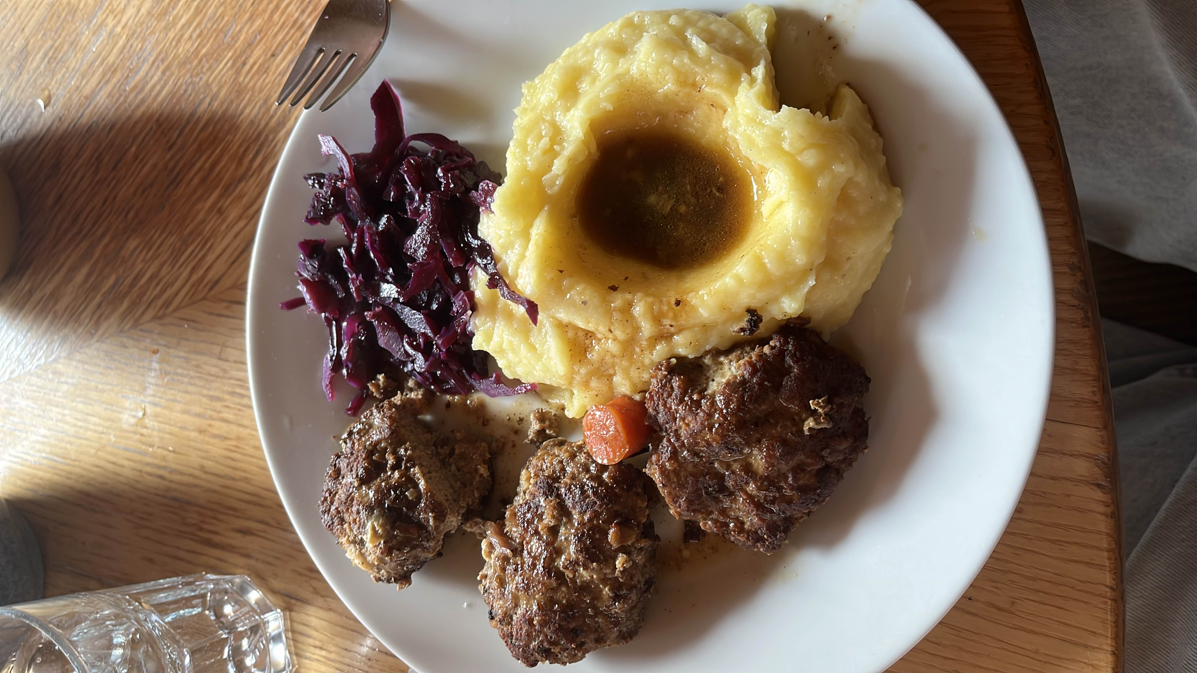 A hearty meal consisting of mashed potatoes with gravy, meatballs, and red cabbage, providing a balanced mix of protein, carbohydrates, and fats.