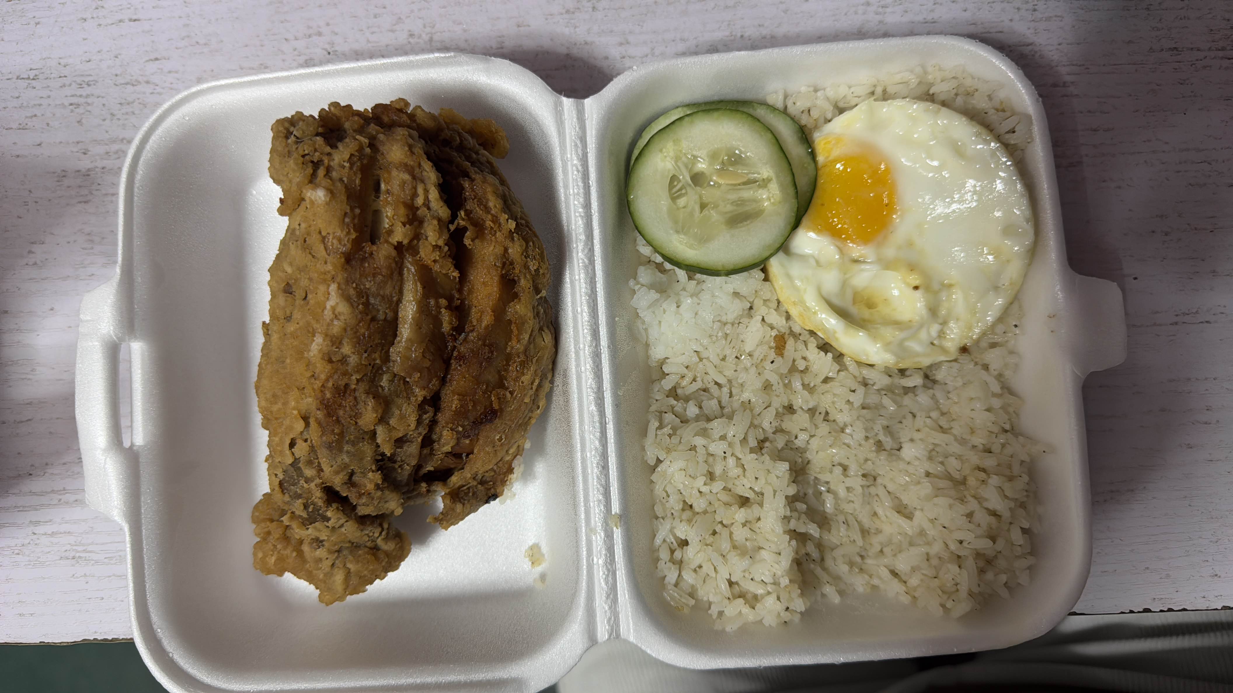 A meal consisting of crispy fried chicken, garlic rice, a fried egg, and cucumber slices, providing a balanced mix of protein, carbohydrates, and fats.