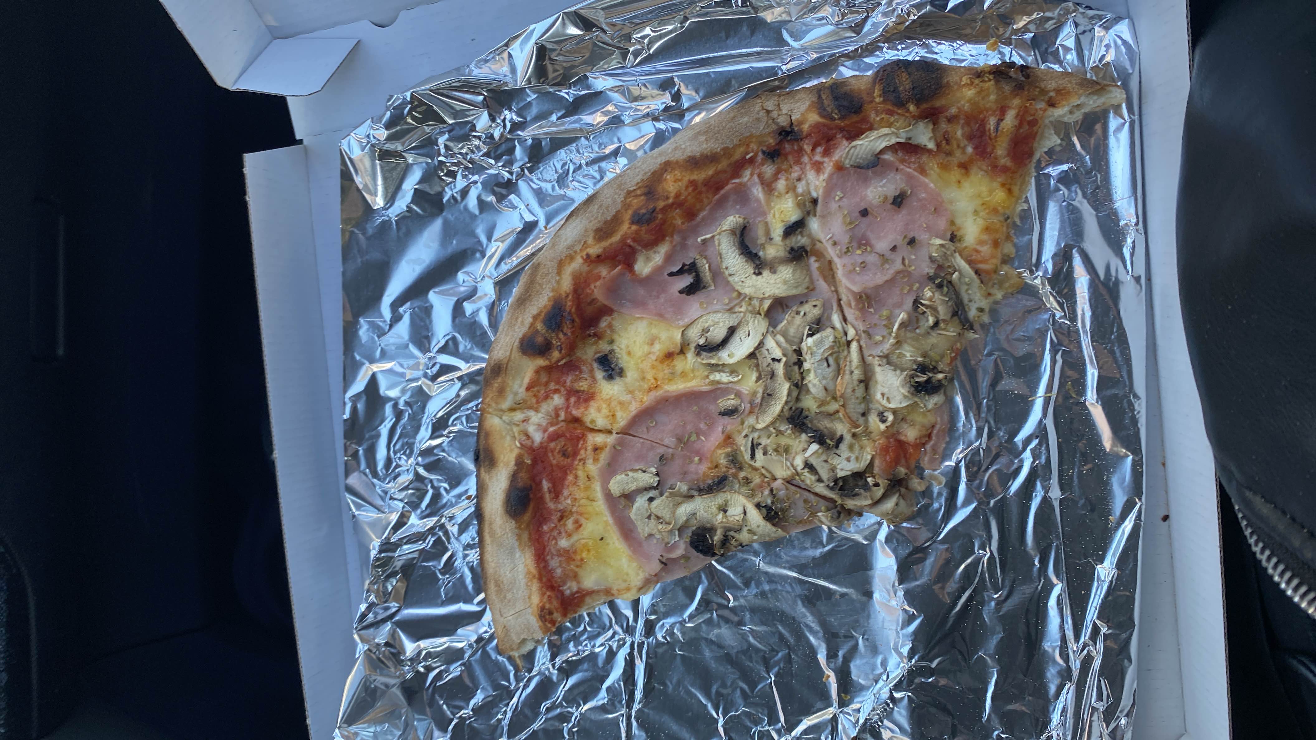 A slice of pizza with ham, mushrooms, cheese, and tomato sauce on a thin crust.