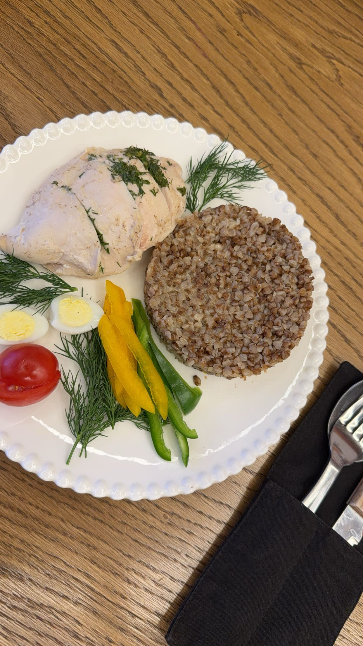 A balanced meal consisting of boiled chicken breast, buckwheat, boiled egg, fresh vegetables, and herbs, providing a high-protein and fiber-rich diet.
