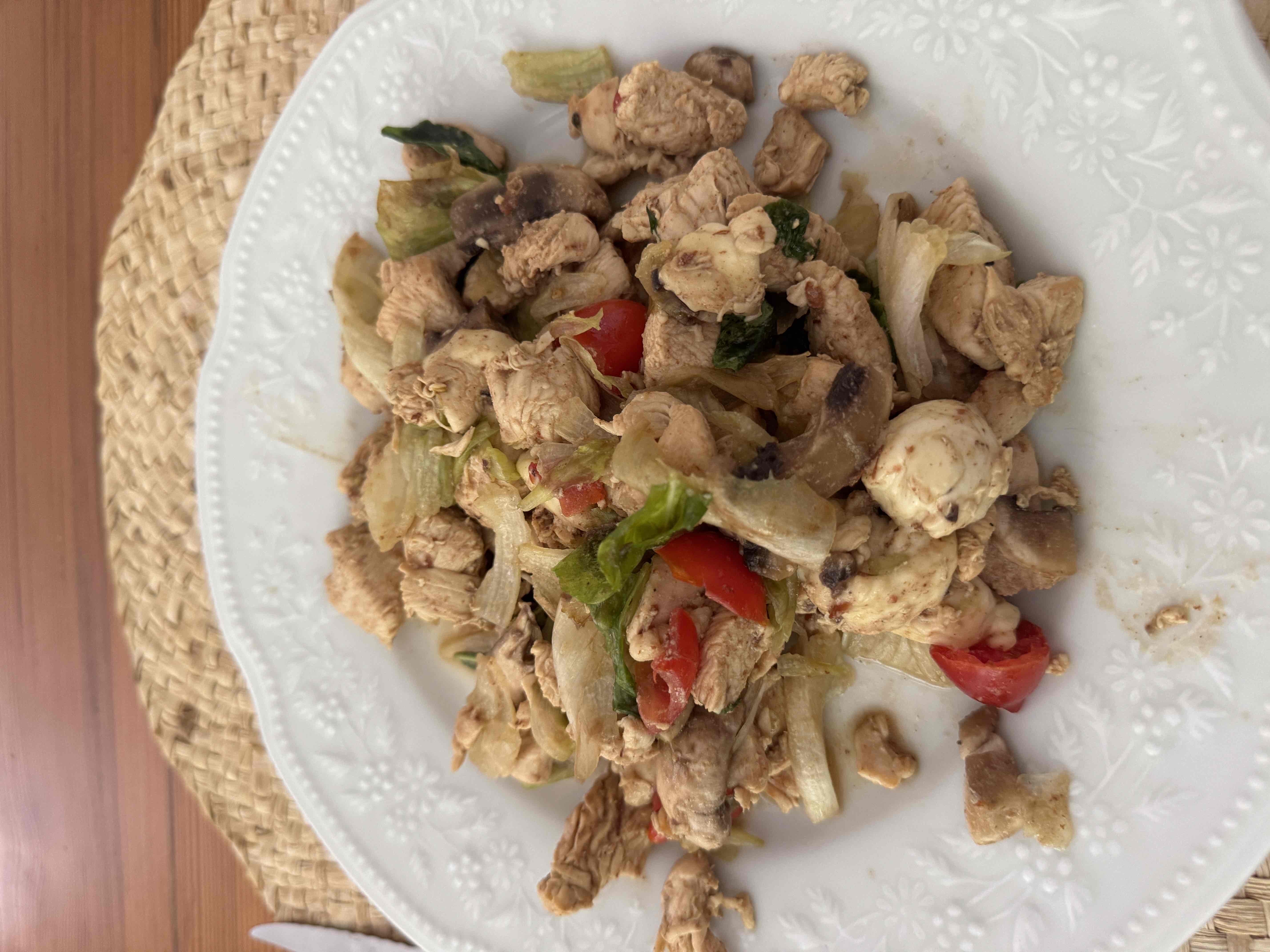 A healthy chicken stir-fry with fresh vegetables including lettuce, cherry tomatoes, mushrooms, and onions, seasoned with spices.