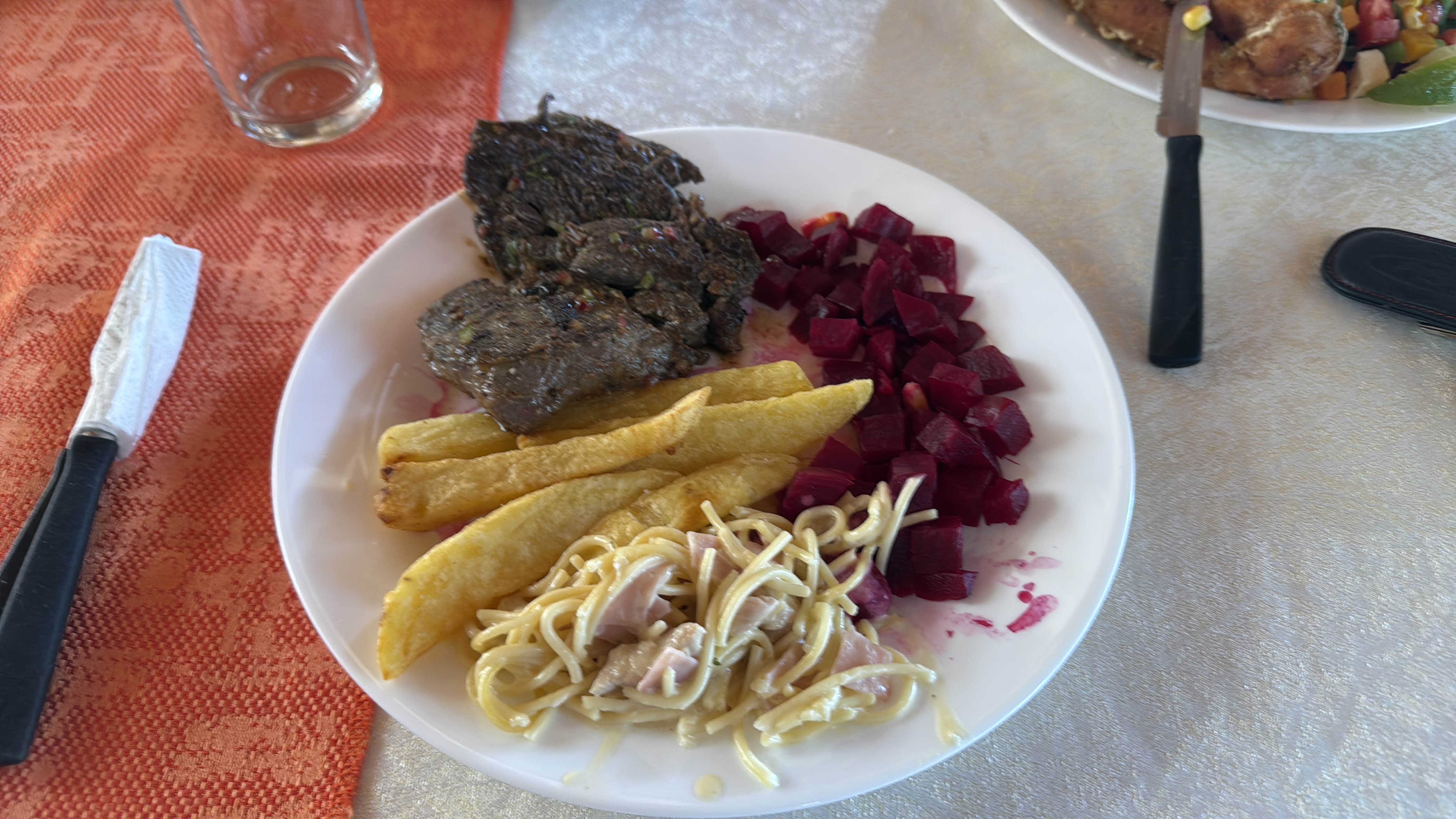 A balanced meal consisting of grilled beef, French fries, pasta with ham and sauce, and beetroot salad, providing a mix of protein, carbohydrates, and fats.