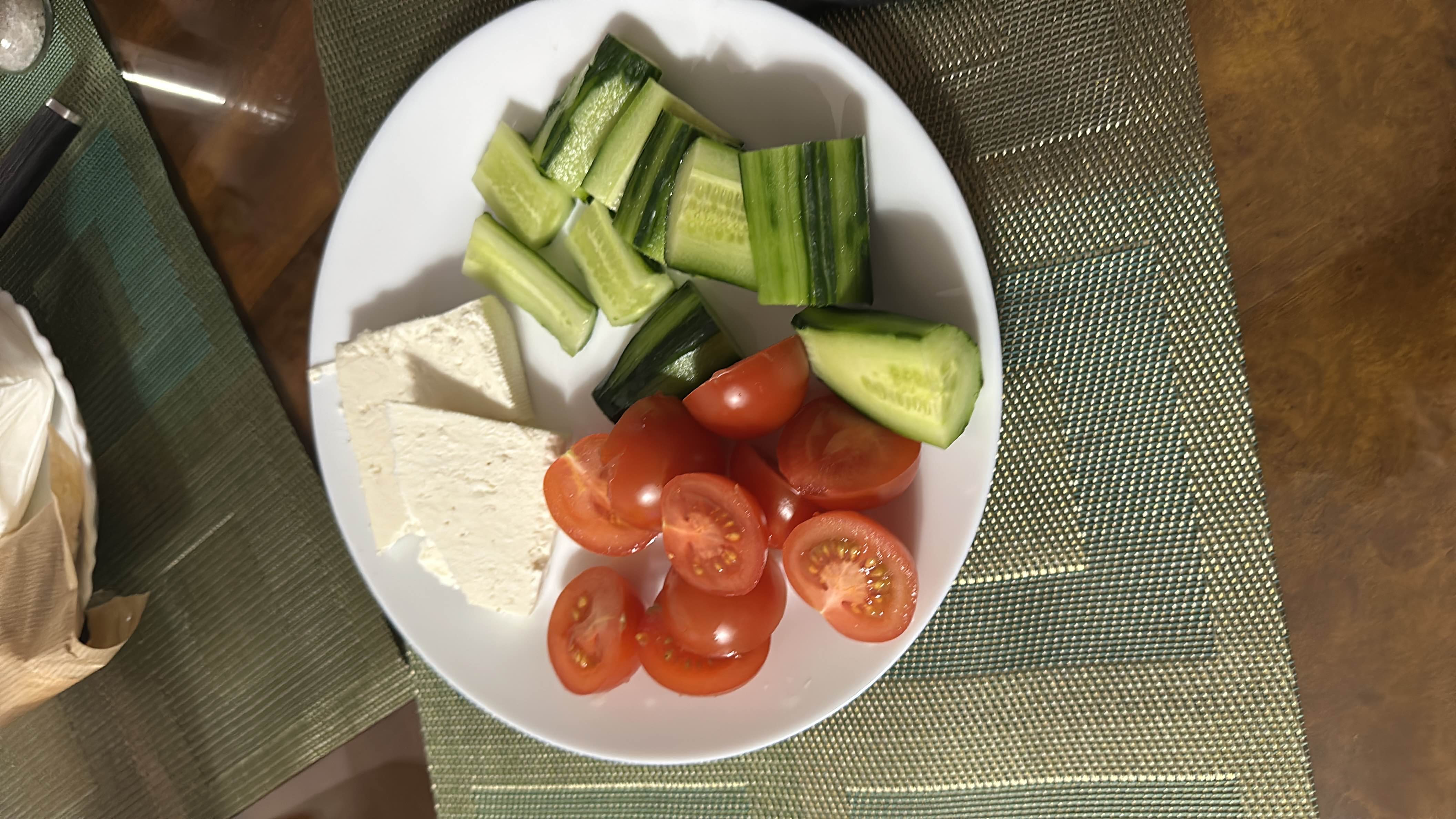 A healthy plate consisting of cherry tomatoes, cucumber slices, and white cheese, providing a balanced mix of protein, carbs, and fats.