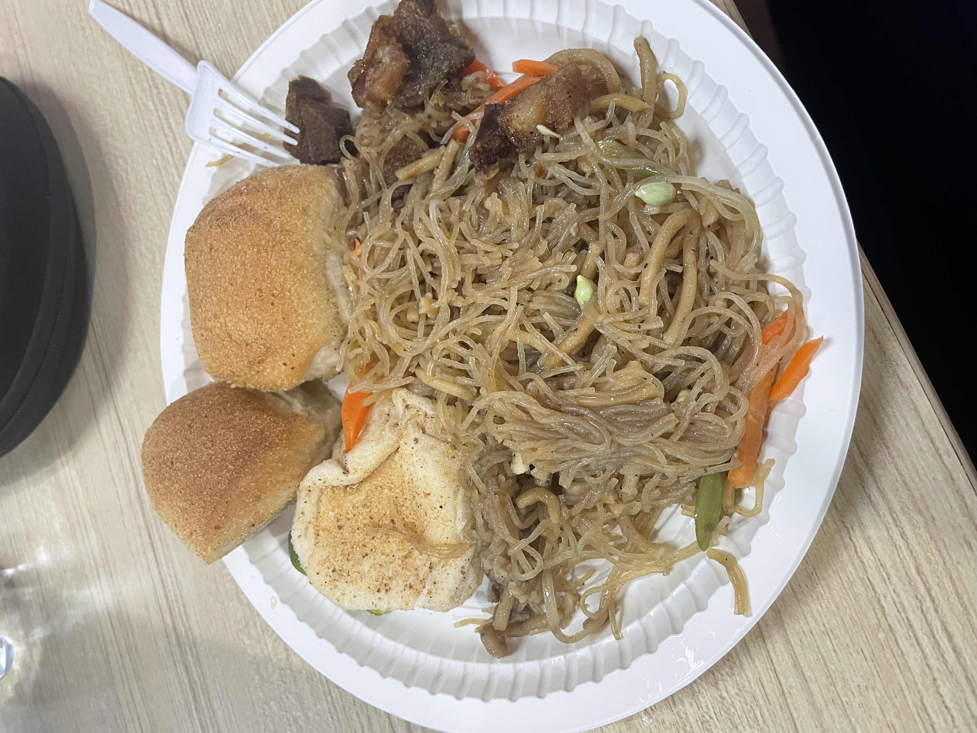 A plate containing stir-fried vermicelli noodles with vegetables, fried meat, and three bread rolls.