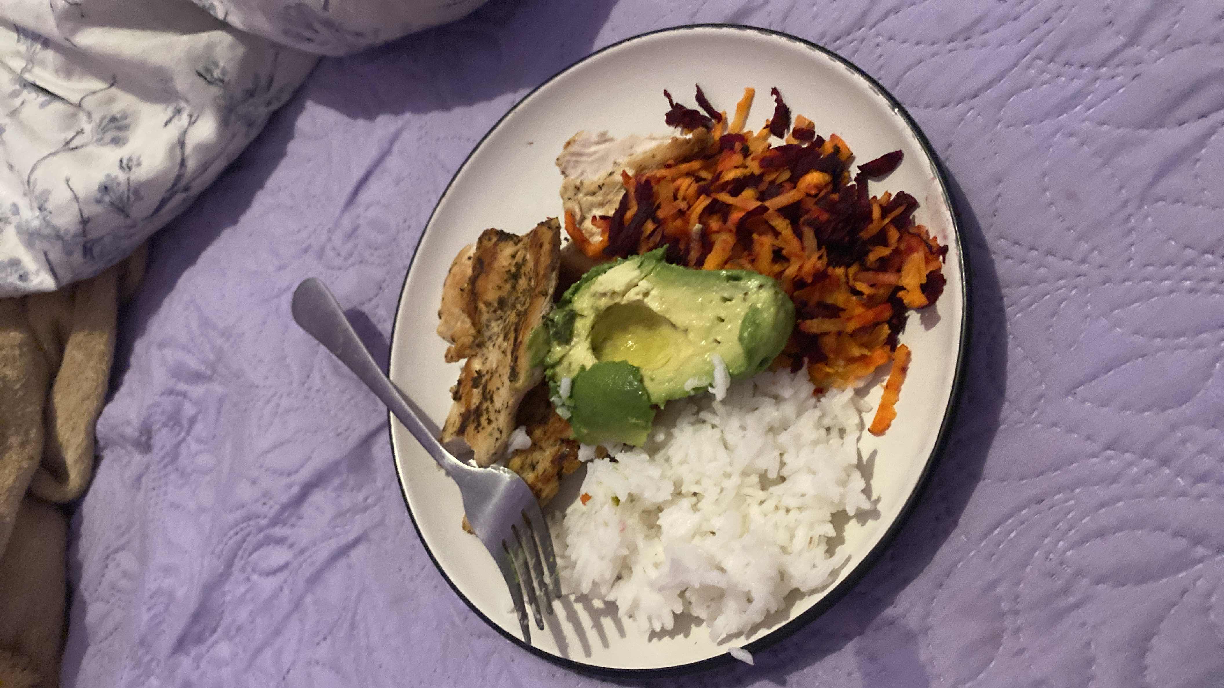 A balanced meal consisting of grilled chicken, white rice, avocado, and grated carrot and beetroot, providing a good mix of protein, healthy fats, and carbohydrates.
