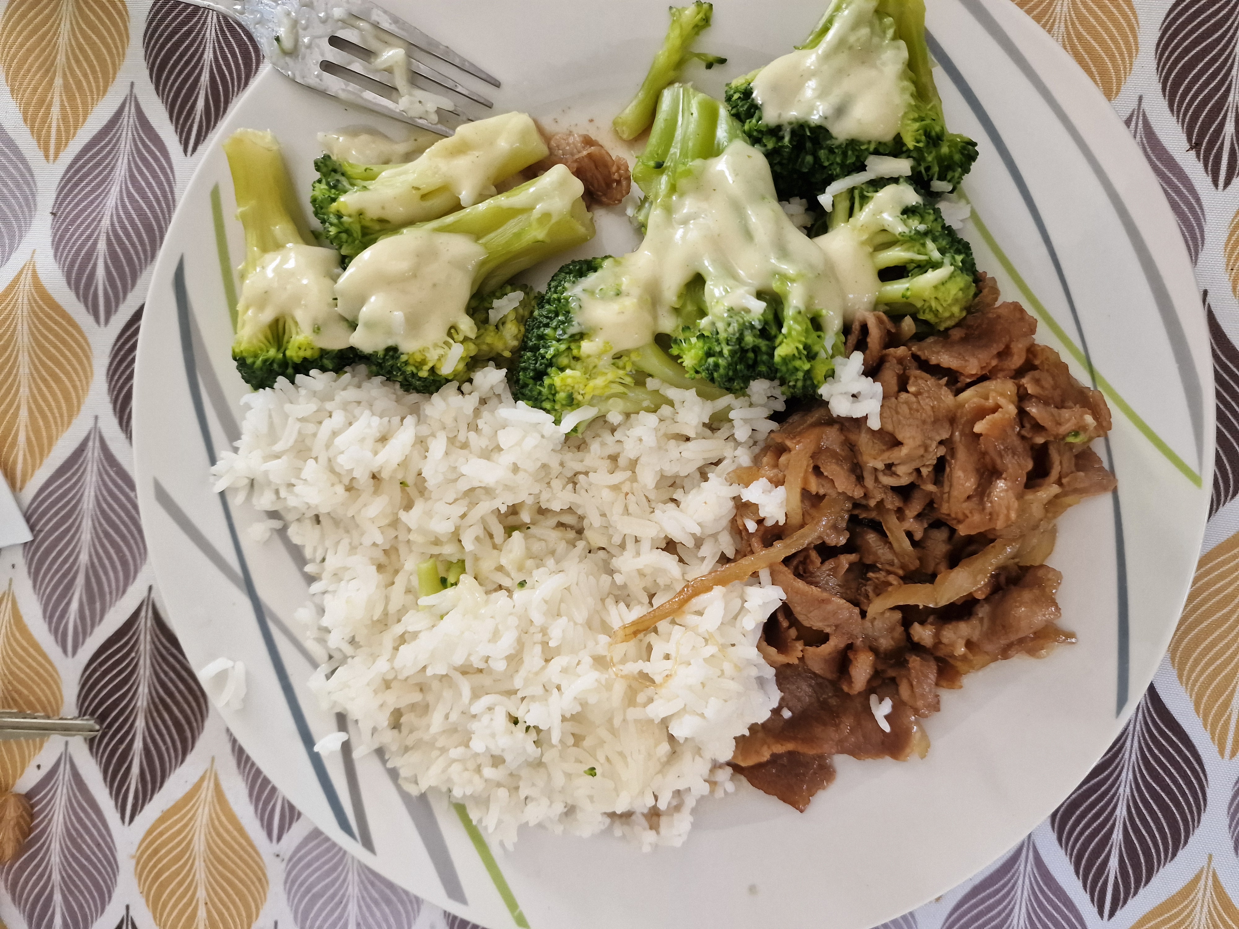 A balanced meal consisting of white rice, stir-fried beef with onions, and steamed broccoli topped with cheese sauce.