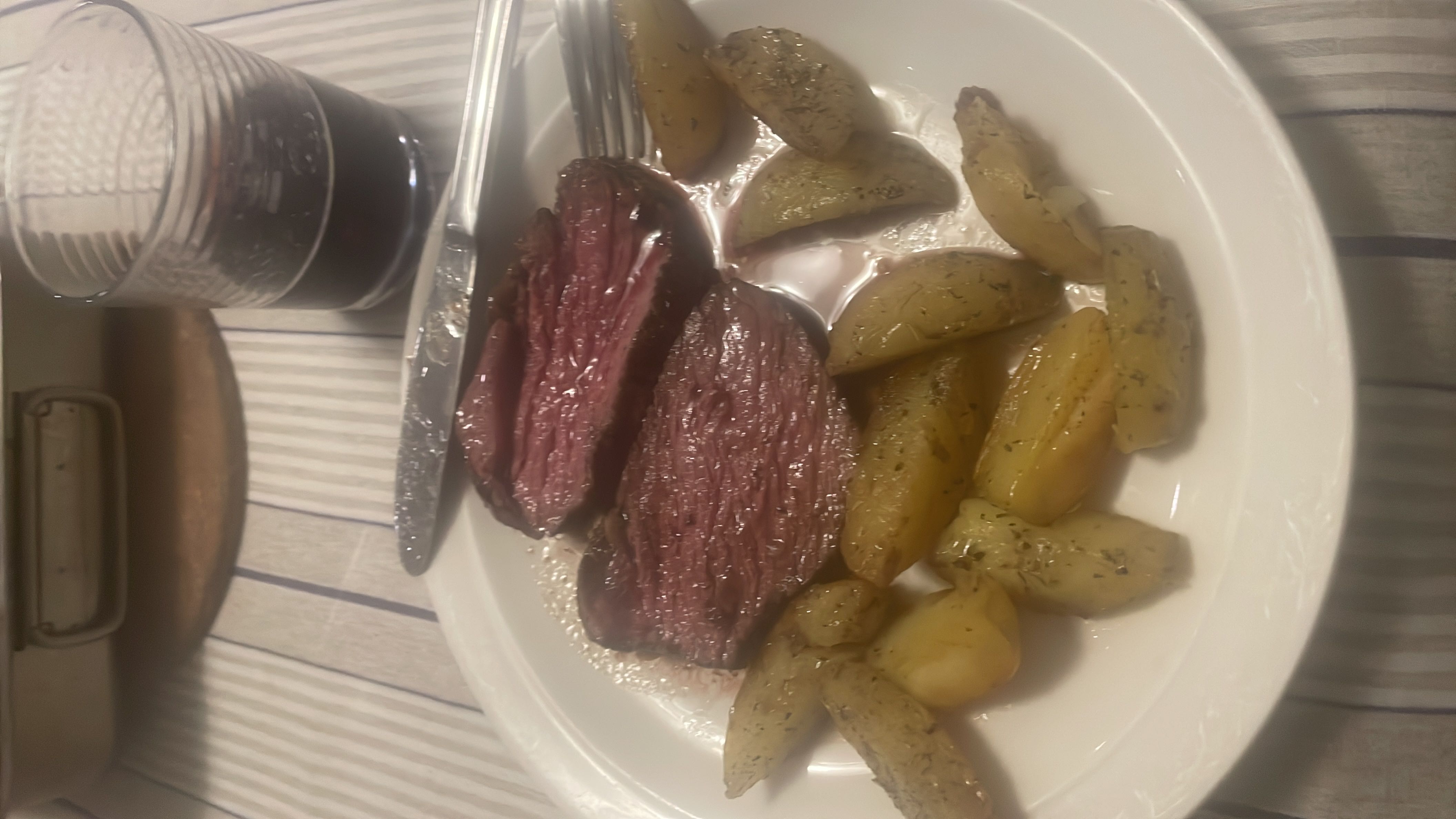 A plate of medium-rare steak served with seasoned roasted potatoes, accompanied by a glass of red wine.