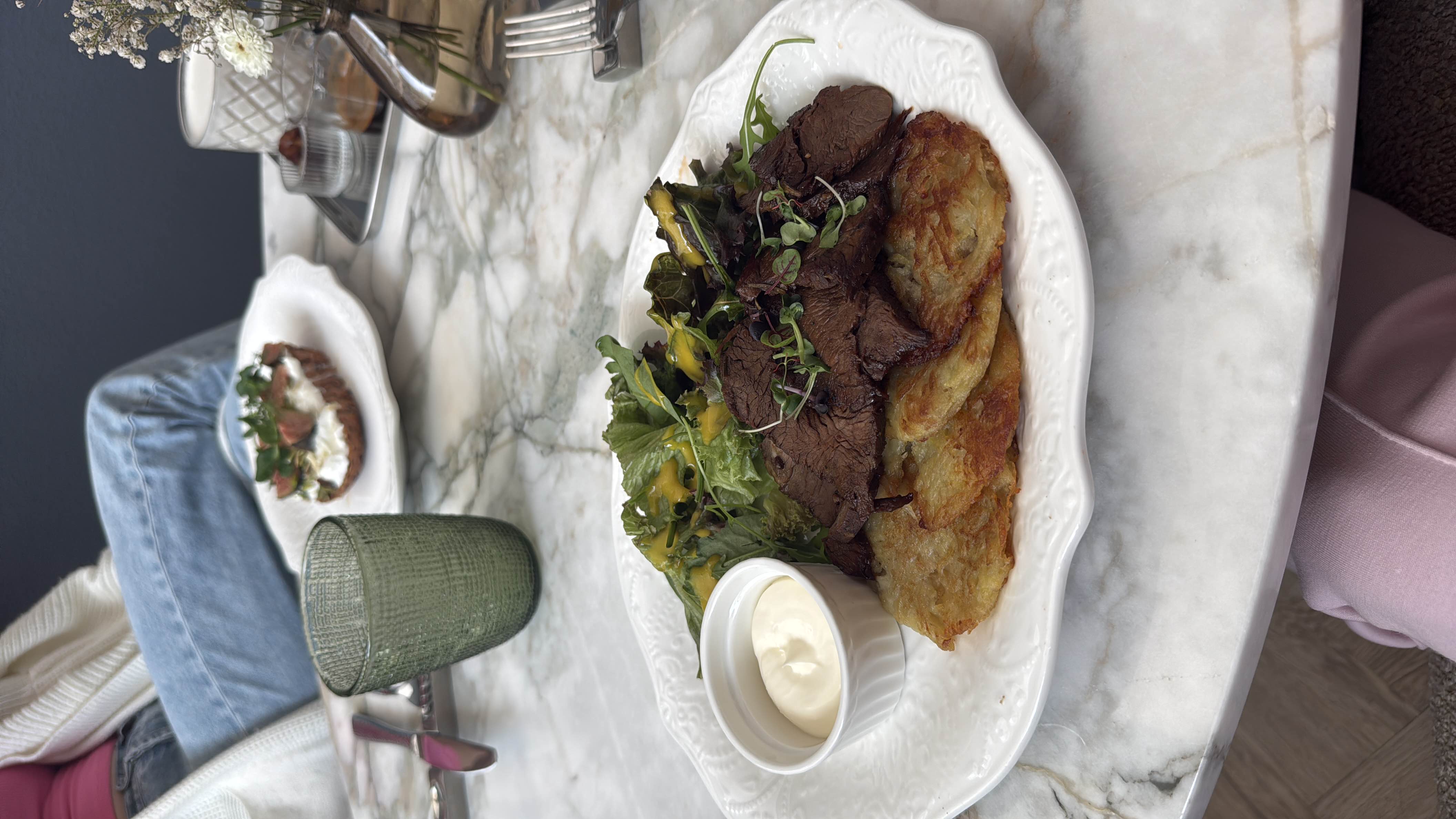 A balanced meal featuring beef slices, crispy potato rosti, fresh mixed greens with dressing, and a side of sour cream.