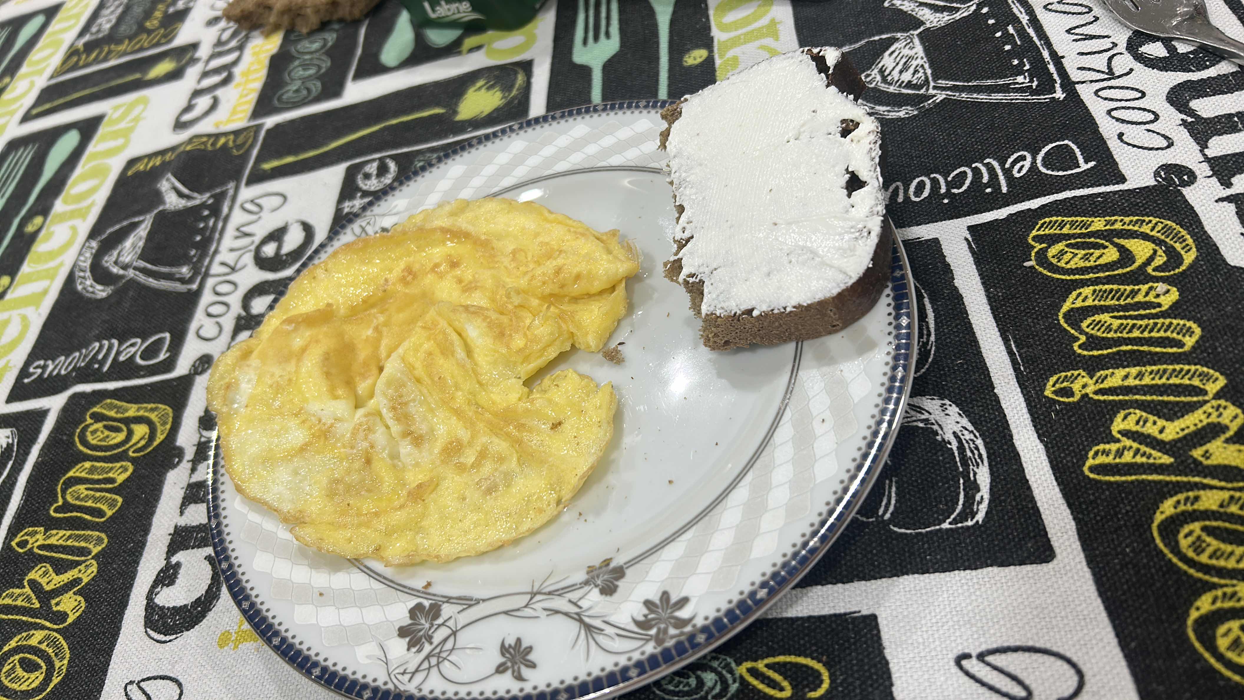 A meal consisting of an omelet and a slice of brown bread with cream cheese, providing a balanced mix of protein, fats, and carbohydrates.