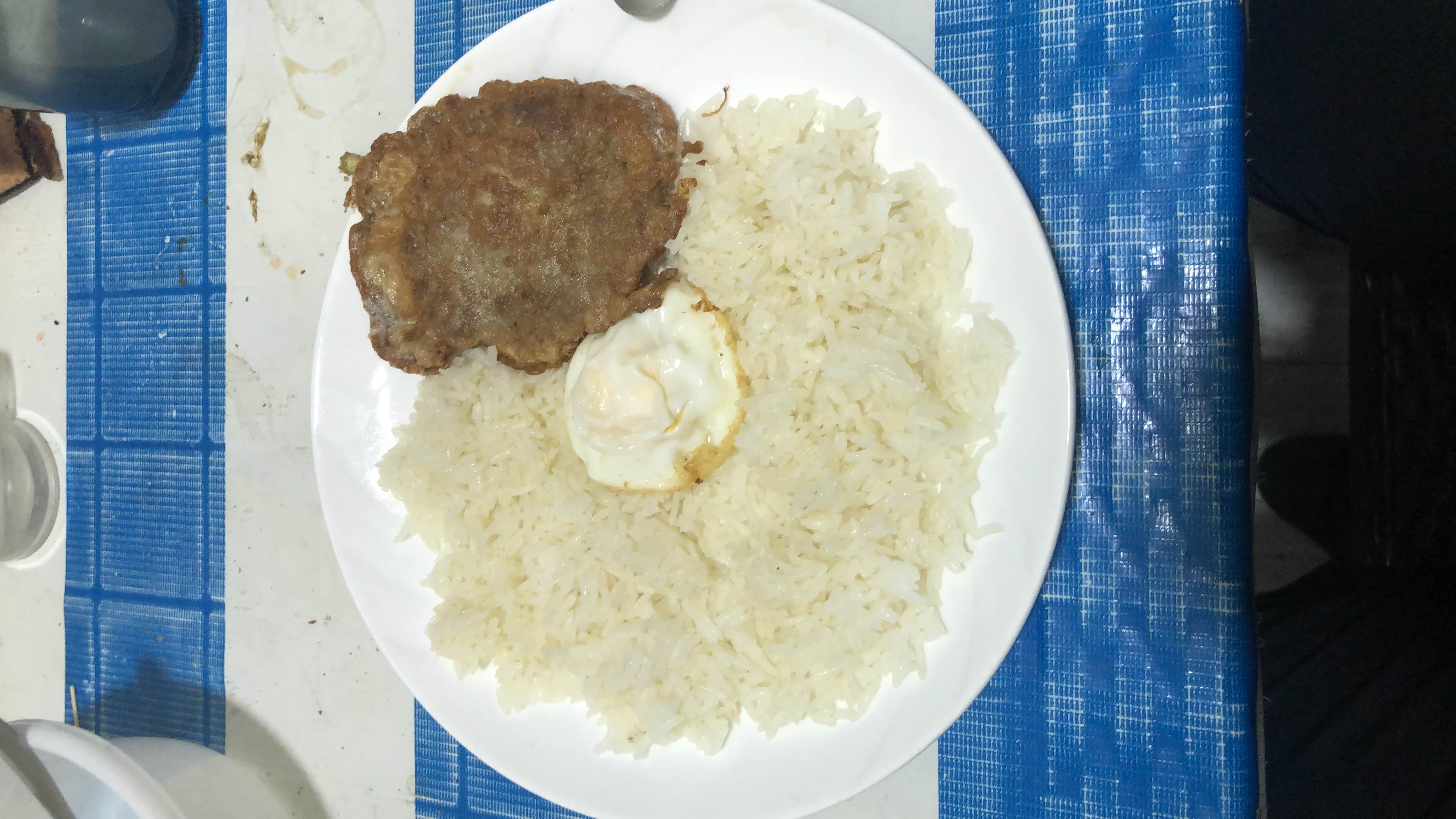 A plate containing white rice, a fried egg, and a breaded meat cutlet, providing a balanced mix of carbohydrates, protein, and fats.