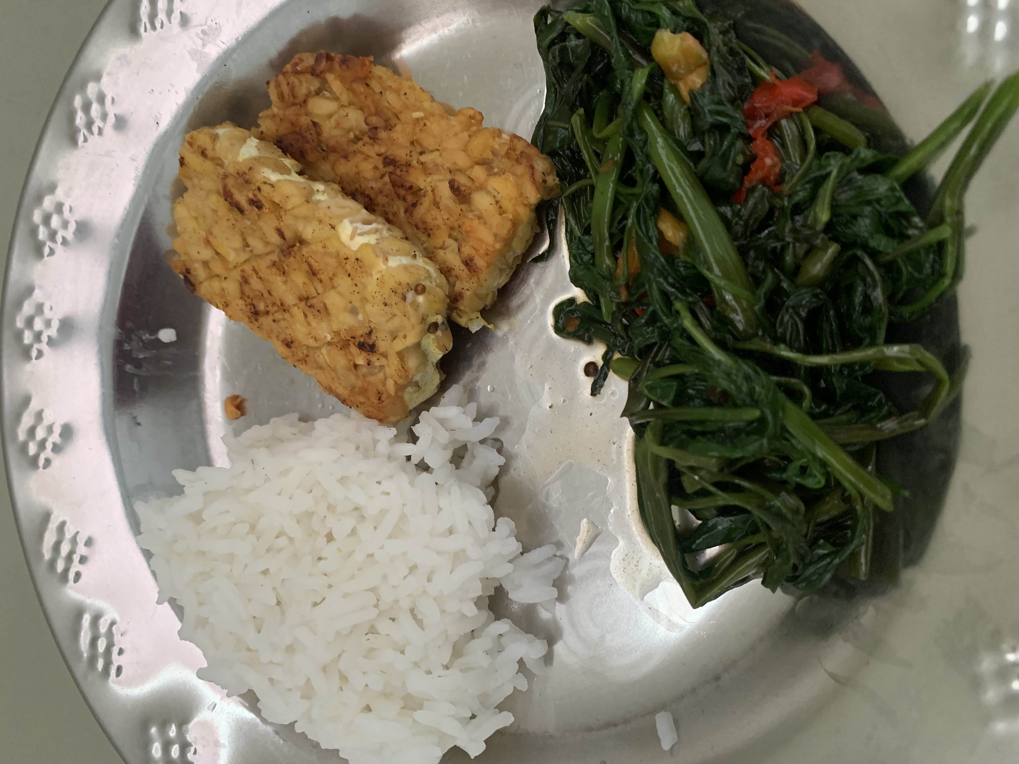 A balanced meal consisting of white rice, grilled tempeh, and stir-fried spinach, providing a good mix of protein, carbohydrates, and fiber.