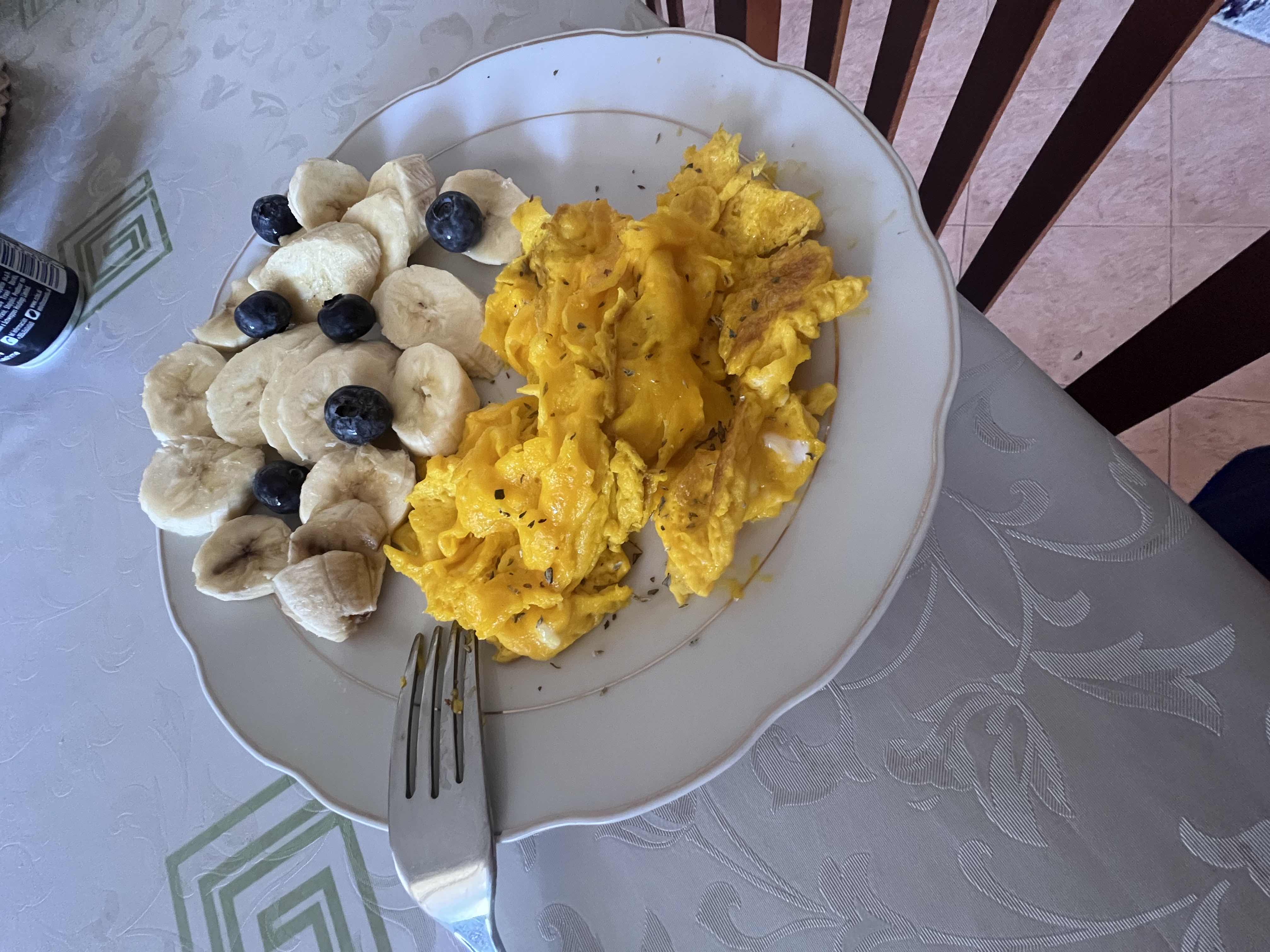 A nutritious meal consisting of scrambled eggs, sliced bananas, and blueberries, providing a balanced mix of protein, carbohydrates, and healthy fats.
