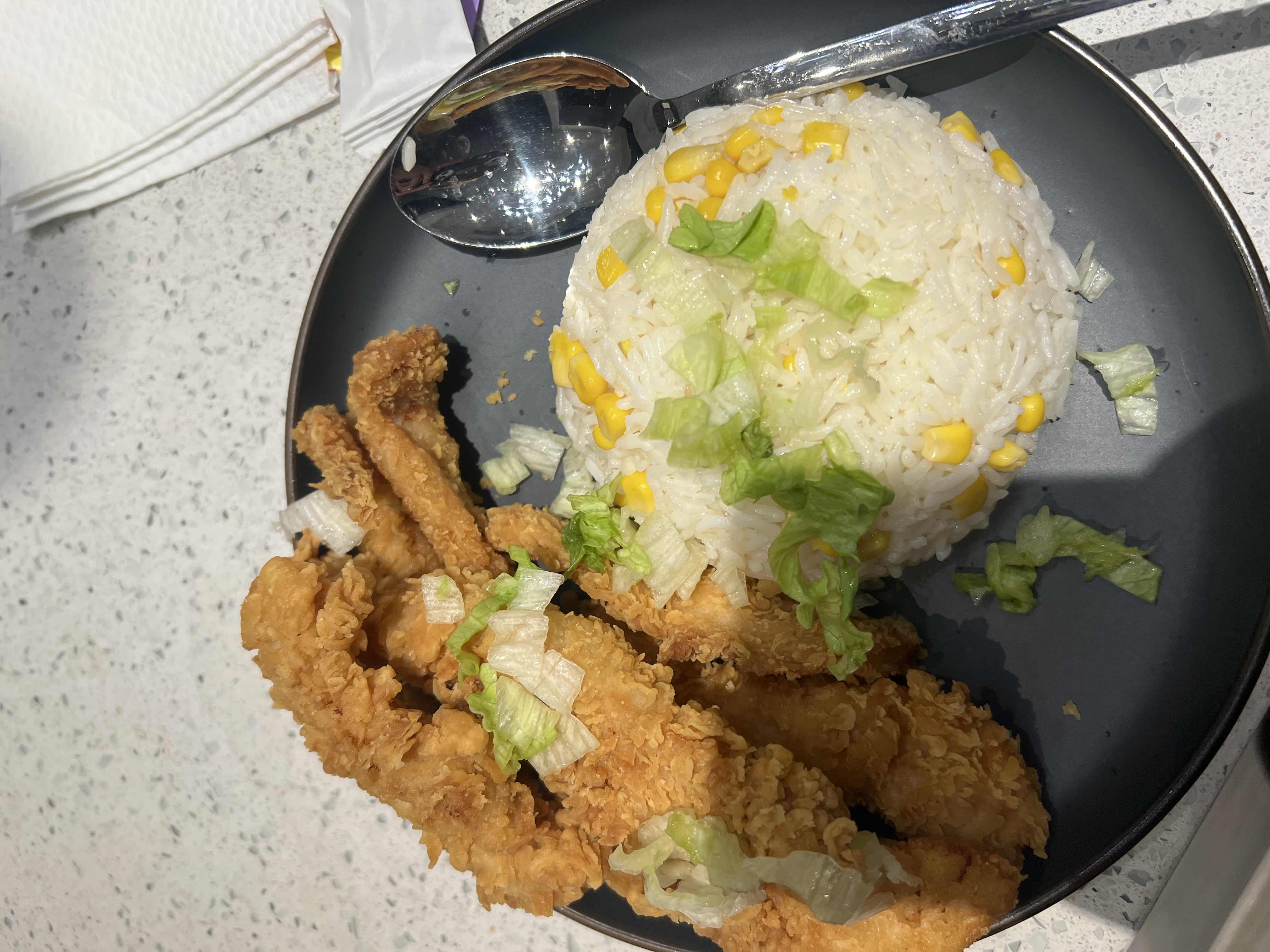 A meal consisting of crispy fried chicken strips, rice mixed with corn, and garnished with fresh lettuce.