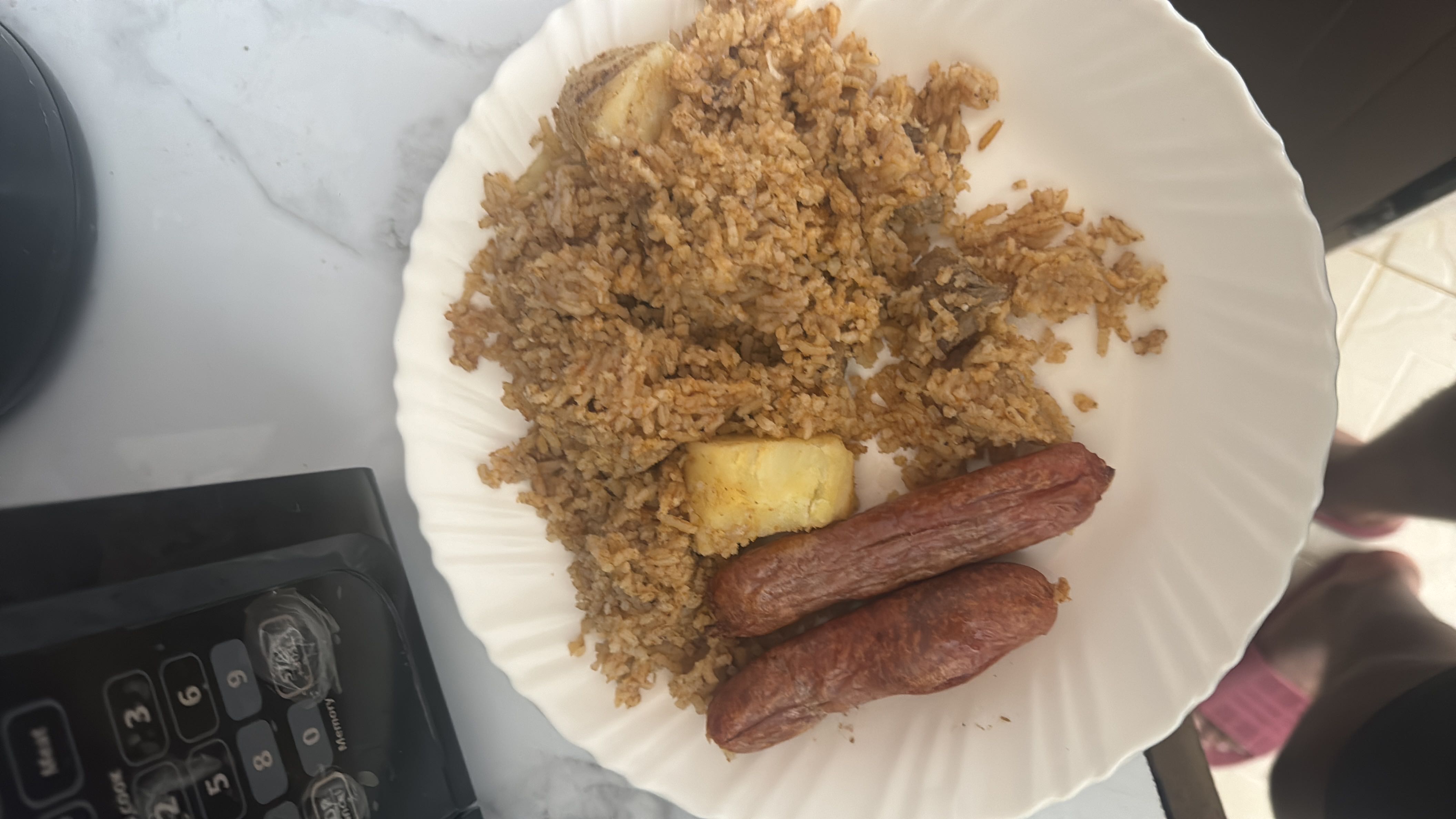 A plate of fried rice with sausages and fried plantain, providing a balanced mix of carbohydrates, proteins, and fats.