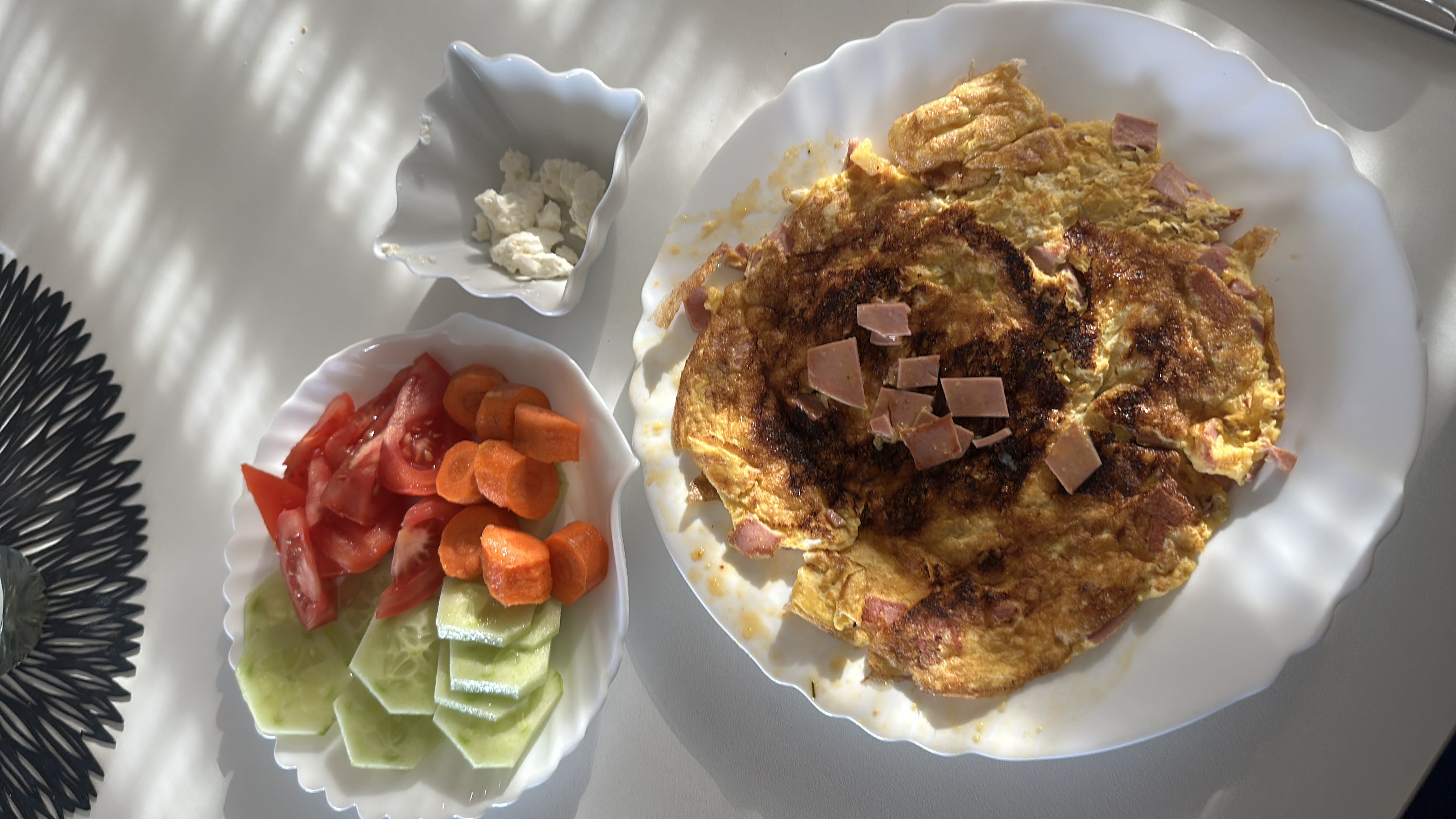 A balanced meal consisting of an omelet with ham, fresh vegetables including tomatoes, cucumbers, and carrots, and a side of cheese.