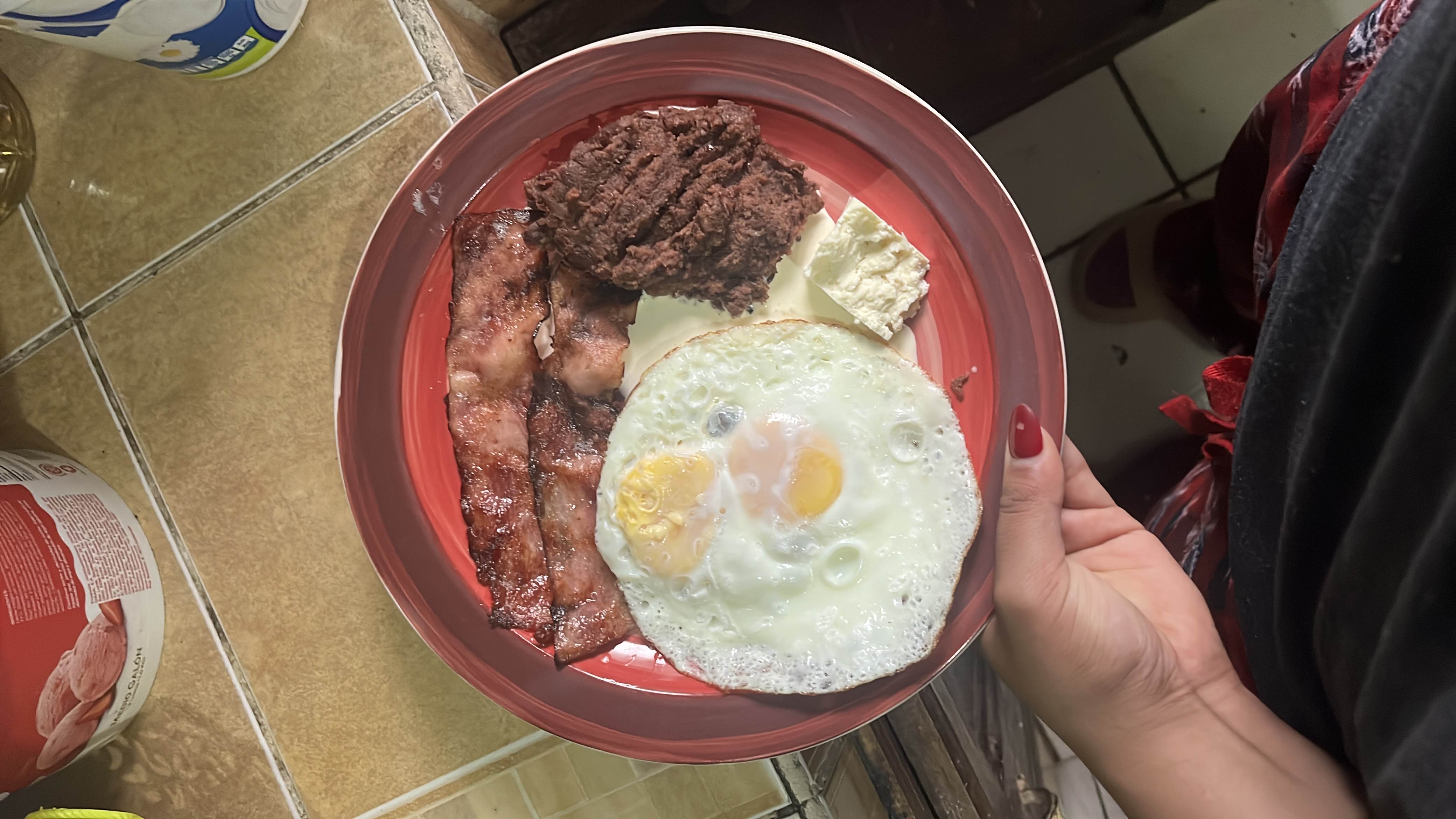 A high-protein breakfast plate featuring fried eggs, crispy bacon, refried beans, and cheese, providing a balanced mix of fats and protein.