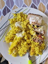 A plate of yellow seasoned rice with grilled fish and a creamy sauce, providing a balanced mix of protein, carbohydrates, and fats.