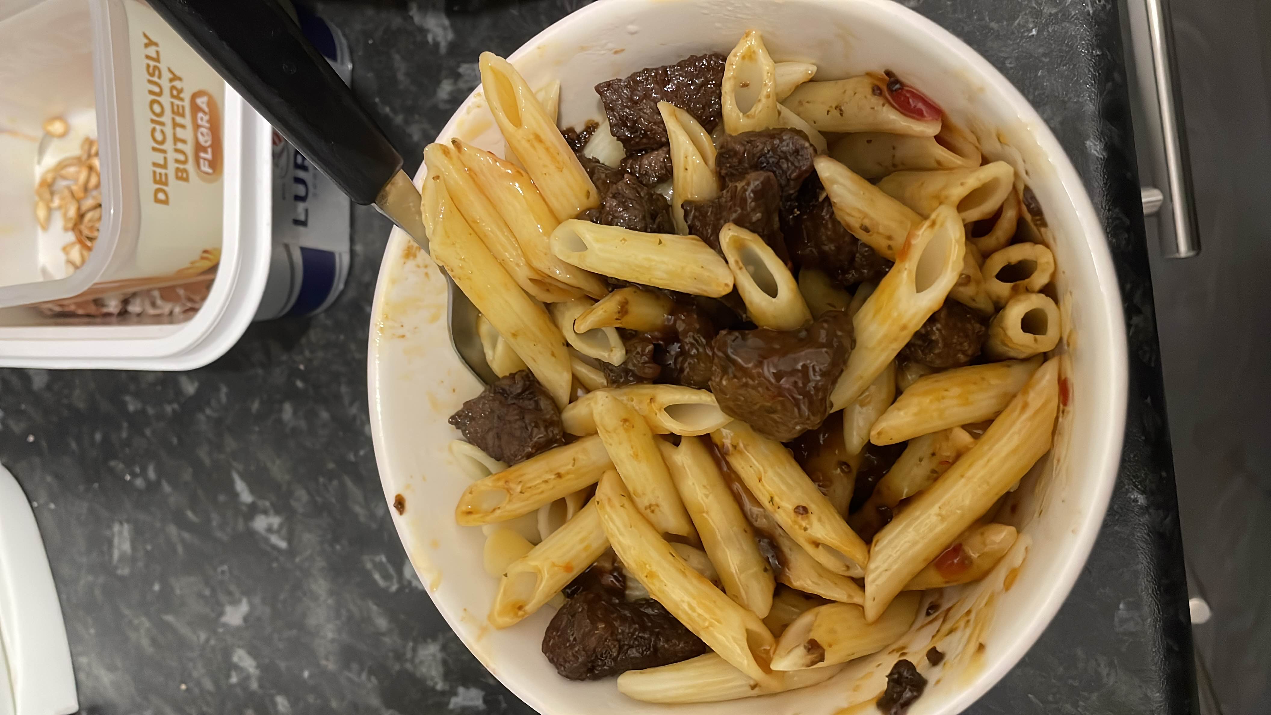 A bowl of penne pasta mixed with beef chunks and a savory sauce, providing a balanced mix of protein, carbohydrates, and fats.