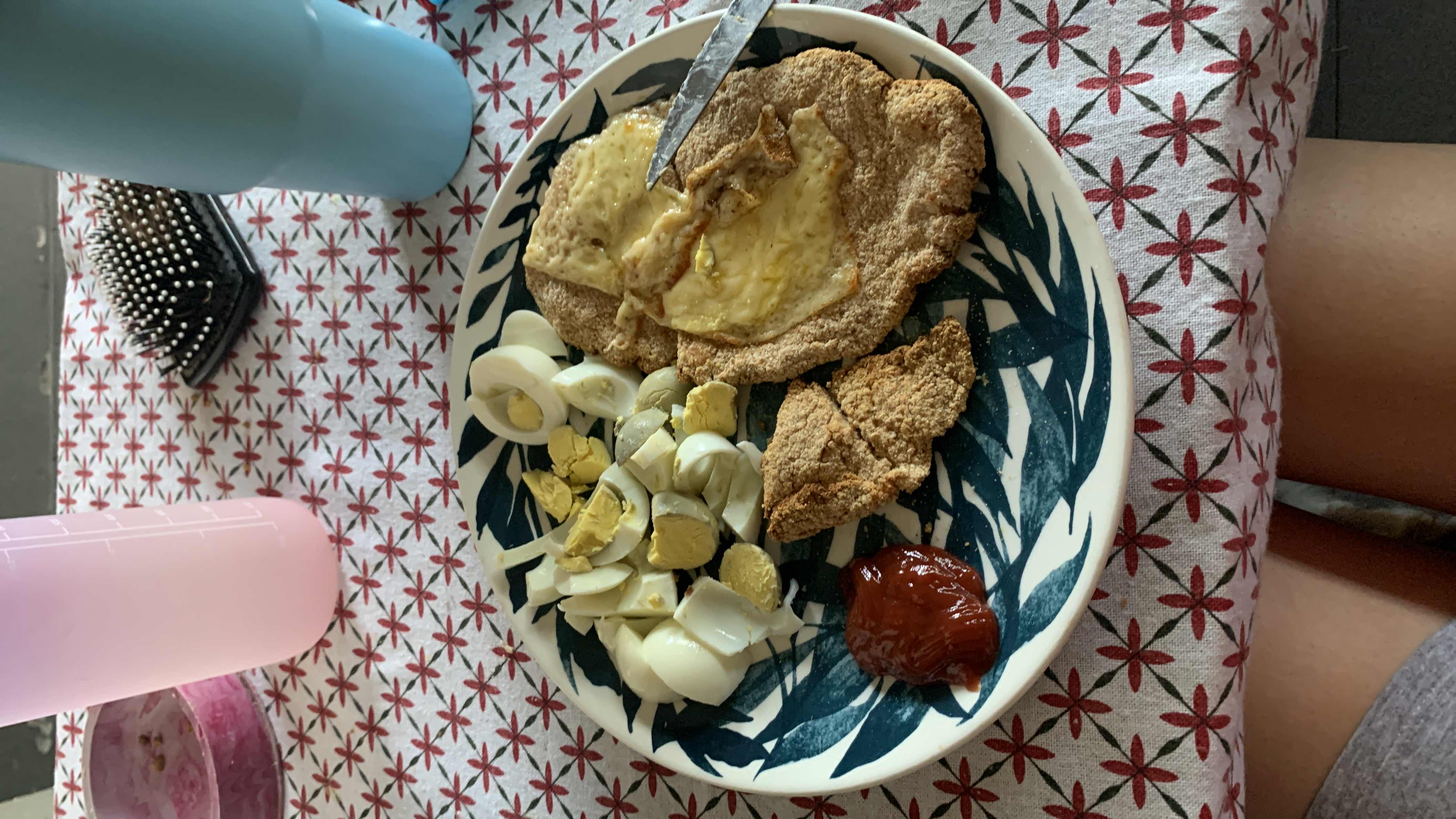 A balanced meal consisting of boiled eggs, whole wheat flatbread with cheese, a baked breaded item, and a small portion of ketchup.